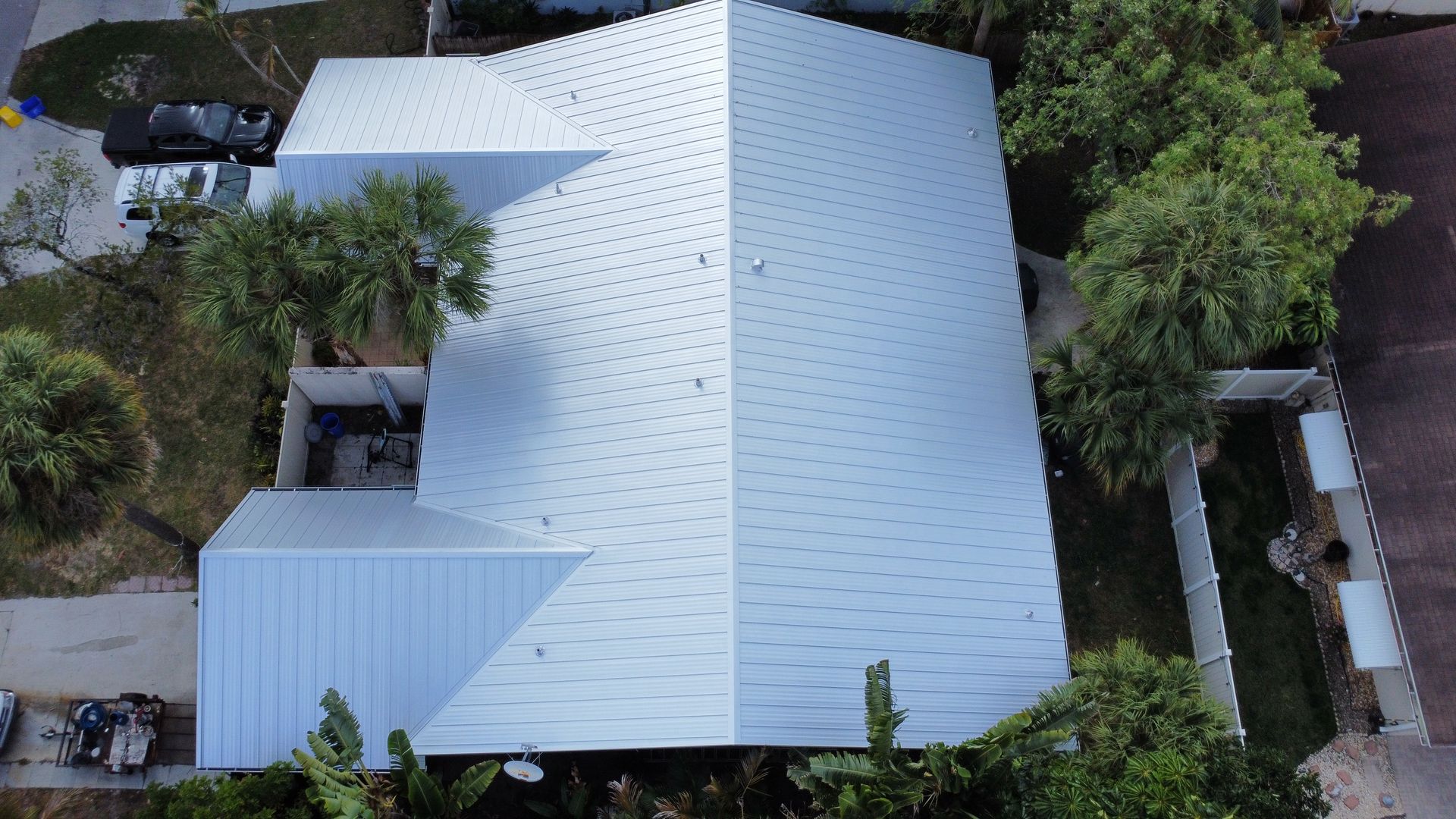 Aerial view of a white metal-roofed house surrounded by dense green trees and a driveway