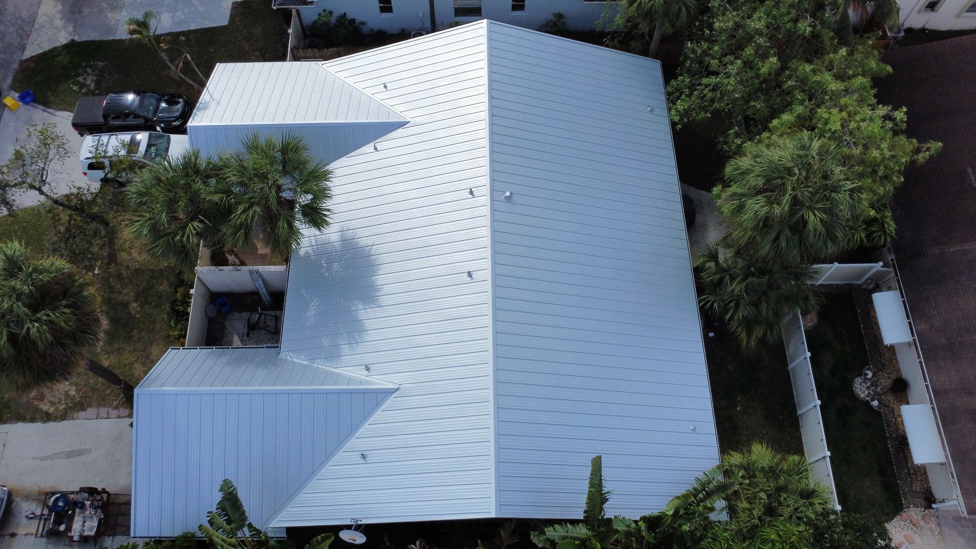 Aerial view of a white metal-roofed house surrounded by trees and a driveway.
