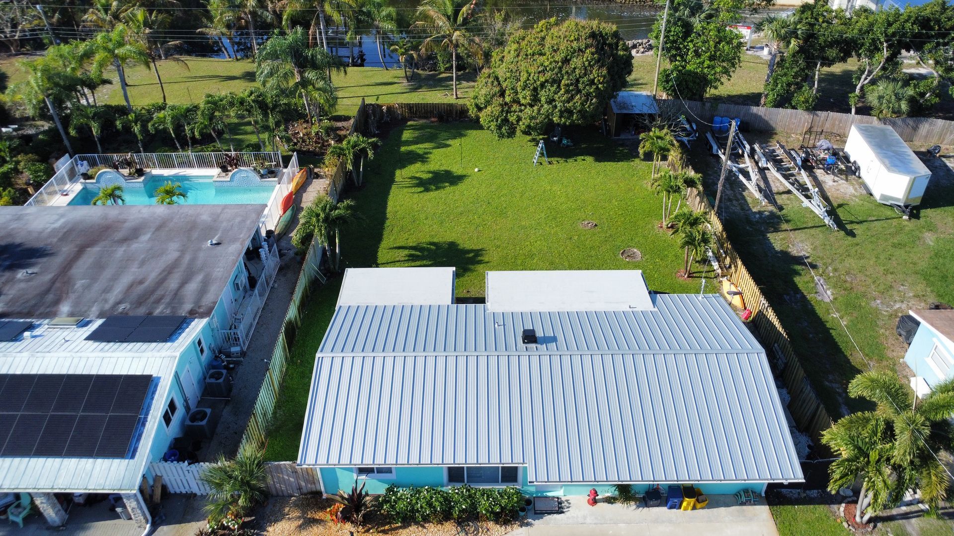 Aerial view of two white-roofed houses with a pool, trees, and a grassy yard in a residential area