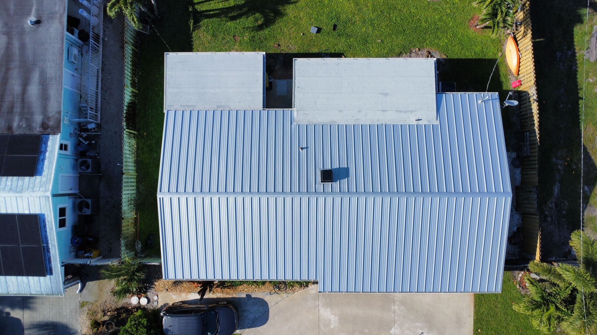 Aerial view of a house with a light gray roof, driveway, and grassy yard.