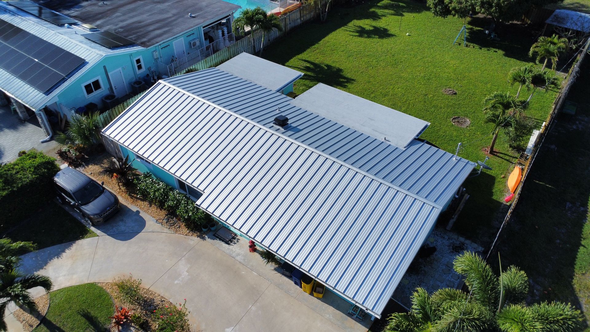 Aerial view of a gray-roofed building beside a grassy yard and paved driveway