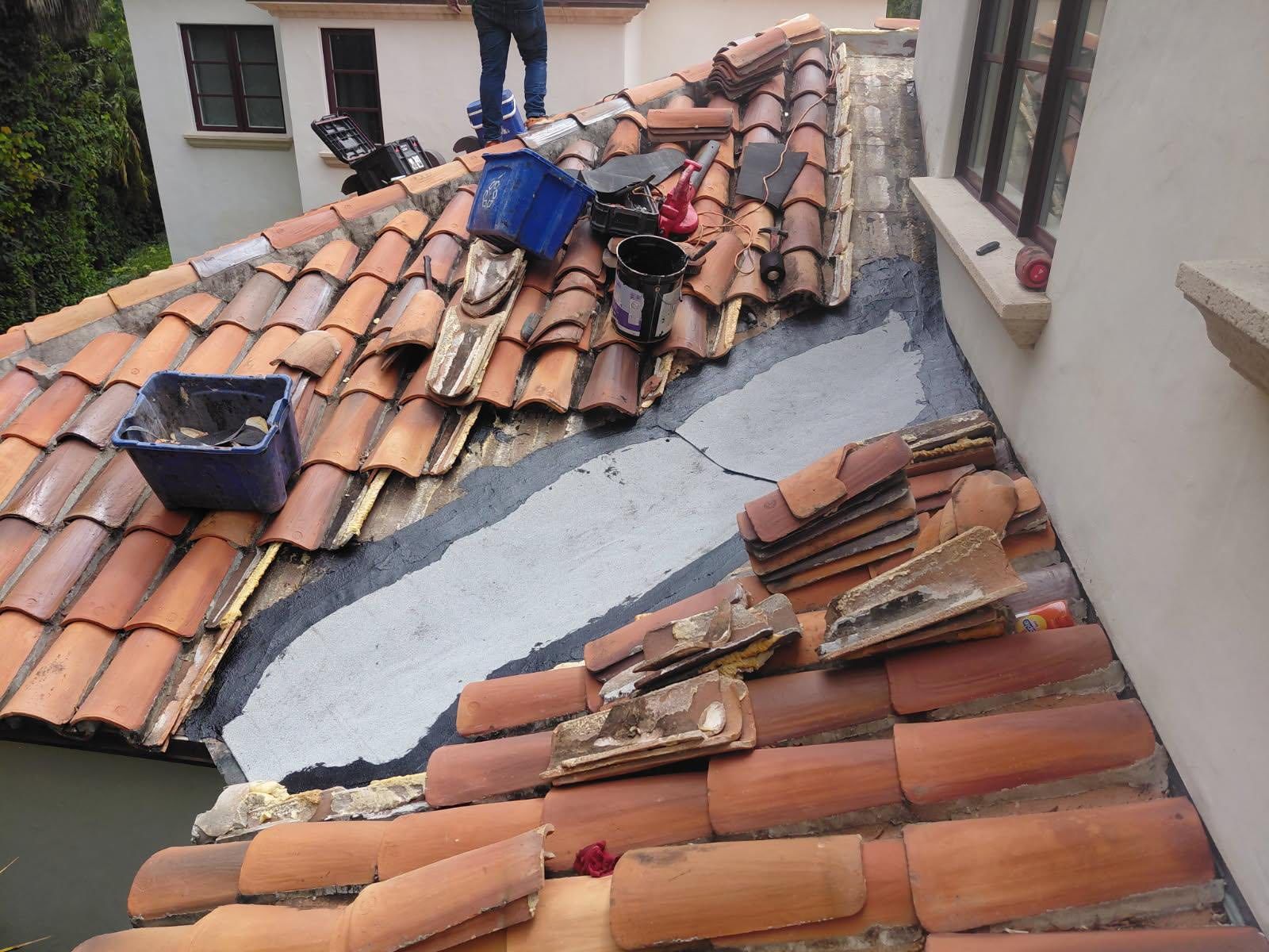 Roof repair on a tiled rooftop, with workers and damaged tiles around a patched section