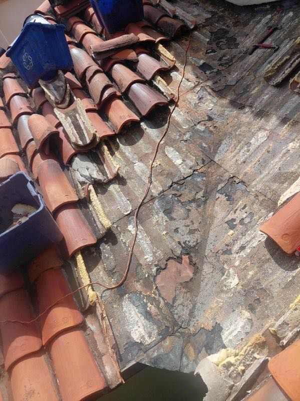 Partially repaired terracotta roof with exposed waterproofing and loose tiles