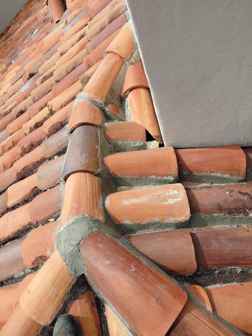 Close-up of red clay roof tiles meeting a gray wall at the roof edge
