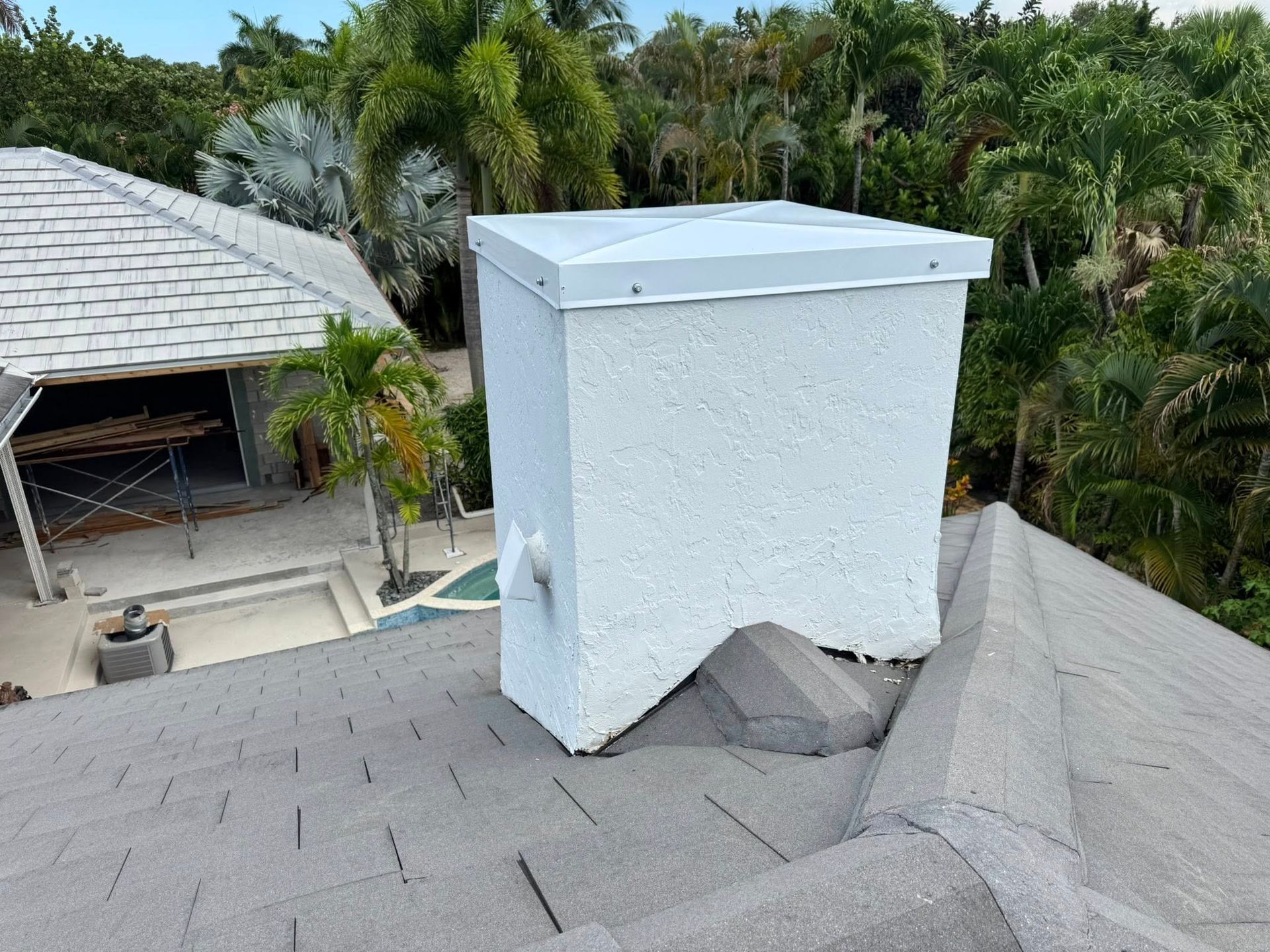 White chimney on a gray shingled roof with tropical trees in the background