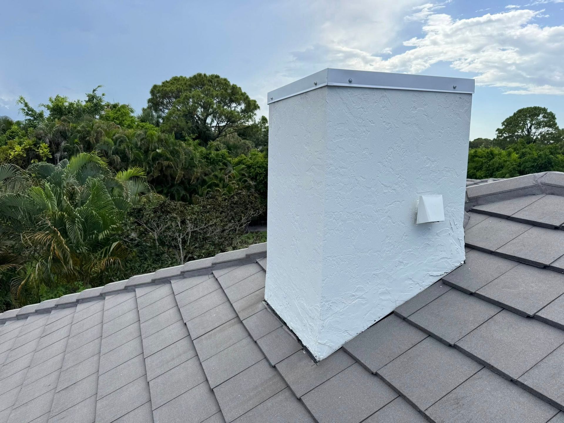 White rooftop chimney vent on gray shingle roof with trees in the background