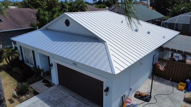 Aerial view of a white house with a gray metal roof and attached garage in a residential neighborhood