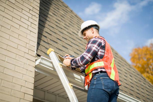 Worker in hard hat and safety vest on a ladder, repairing the roof of a brick building.