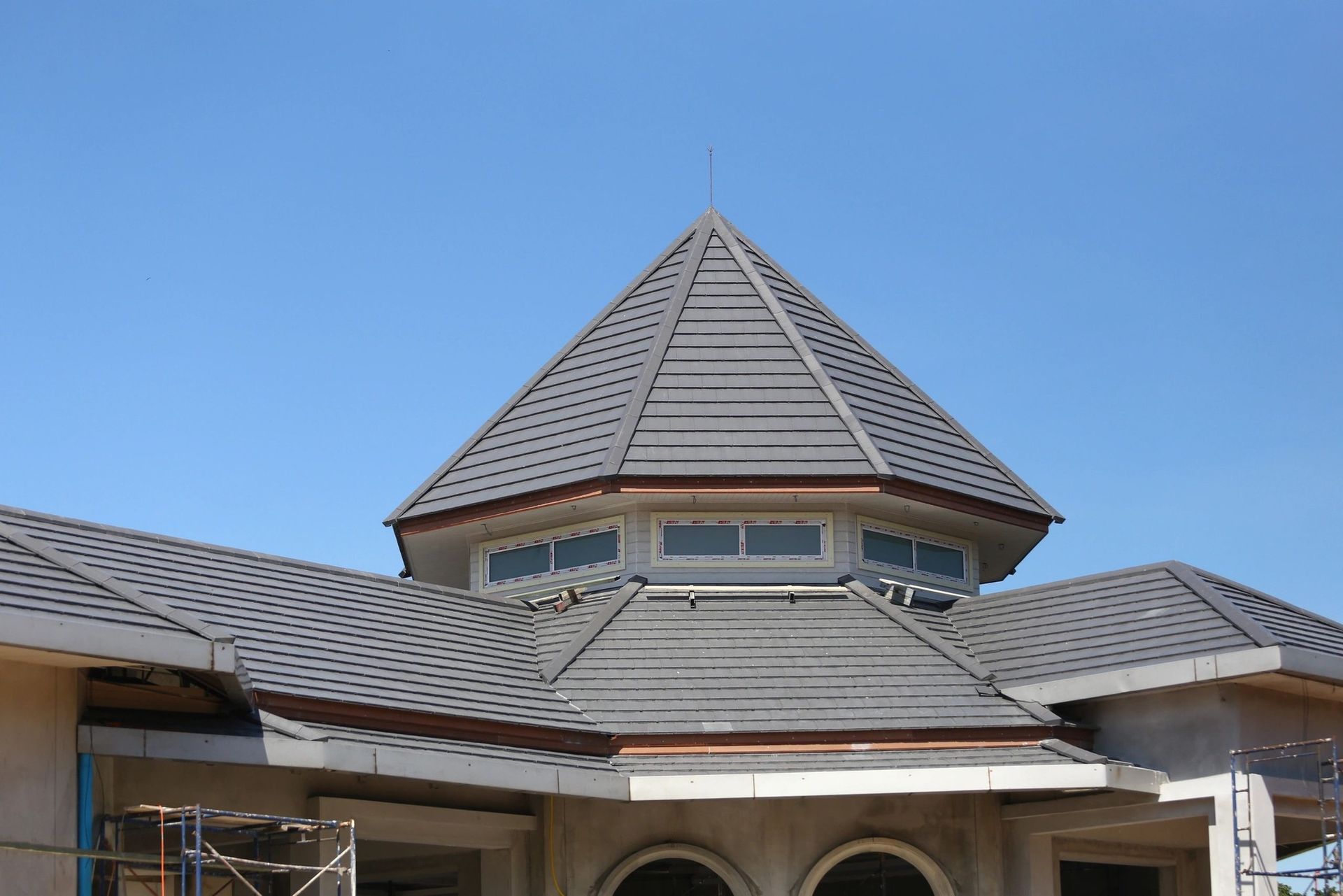 Building roof with gray shingles and a central conical turret against a blue sky