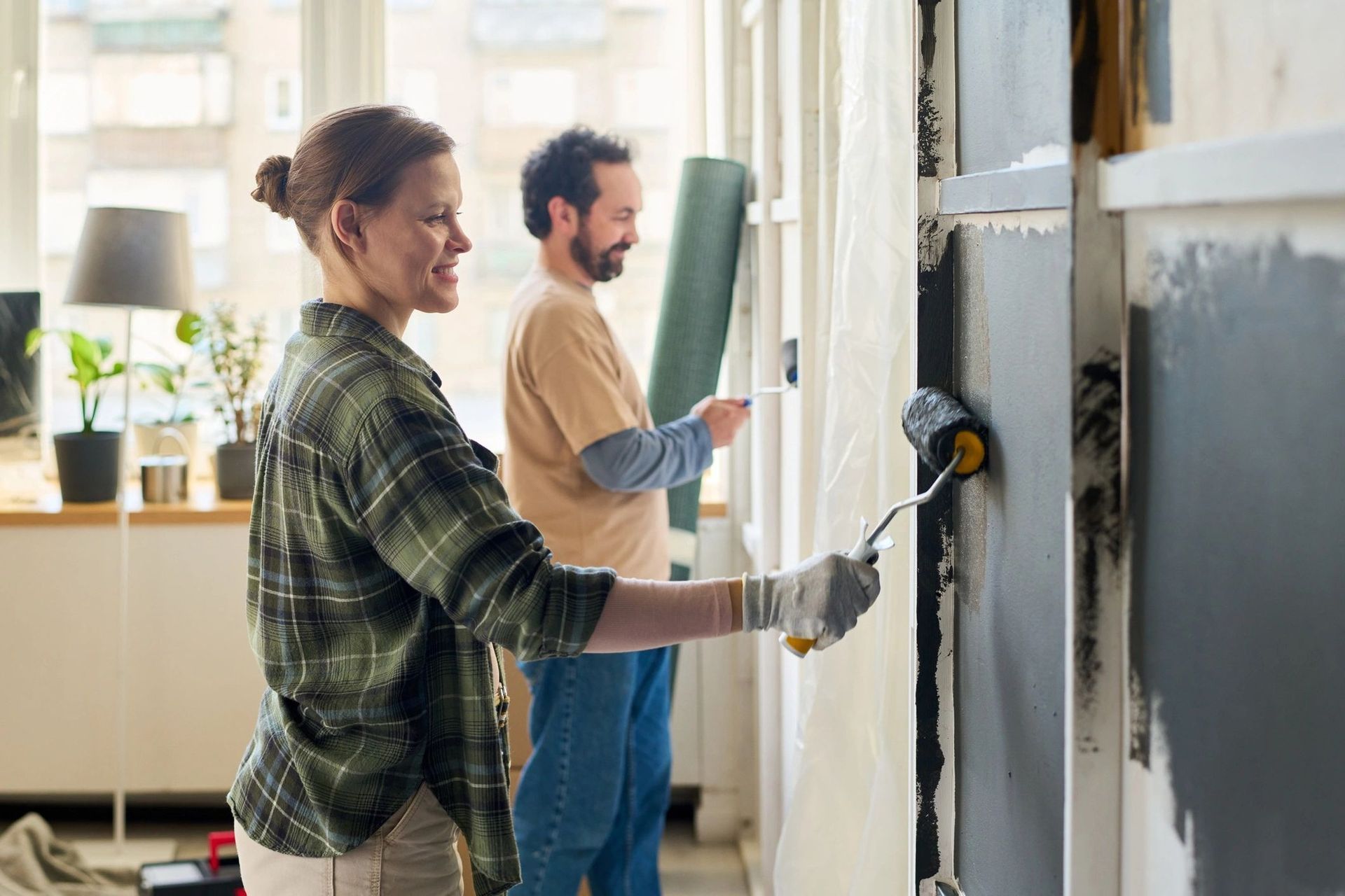 Two people painting a wall in a bright room, one using a roller and the other a brush.