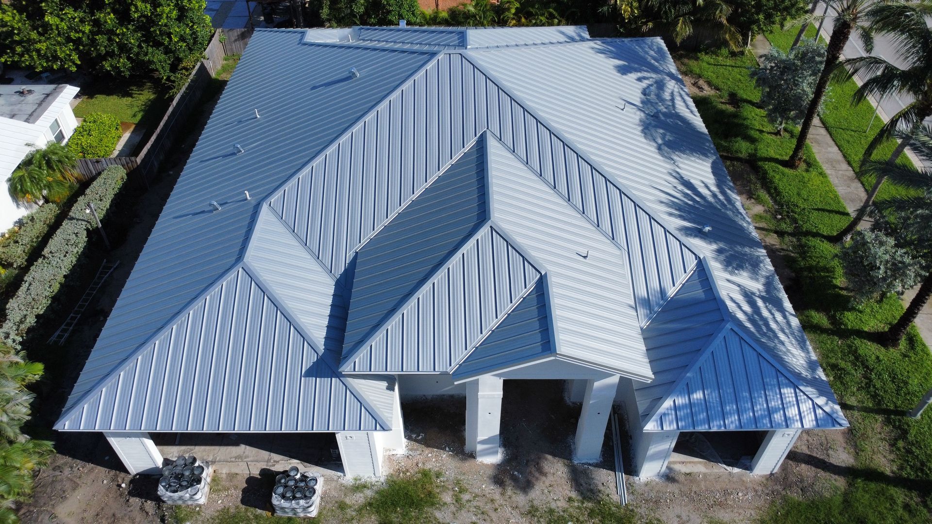 Aerial view of a modern house with a gray metal roof and centered dormers, surrounded by trees.