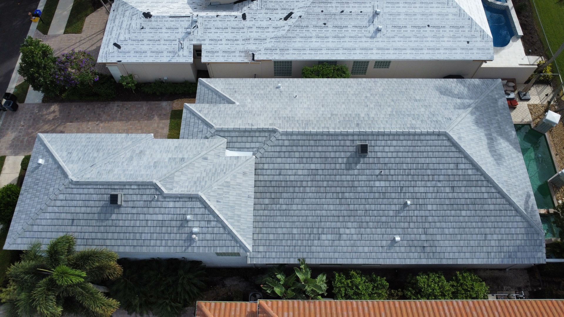 Aerial view of two gray shingle rooftops on suburban houses with surrounding trees and fences