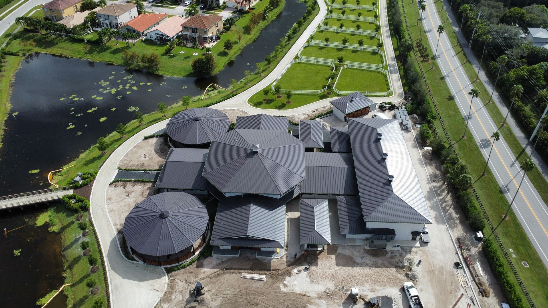 Aerial view of a modern building complex beside a pond, road, and grassy grounds