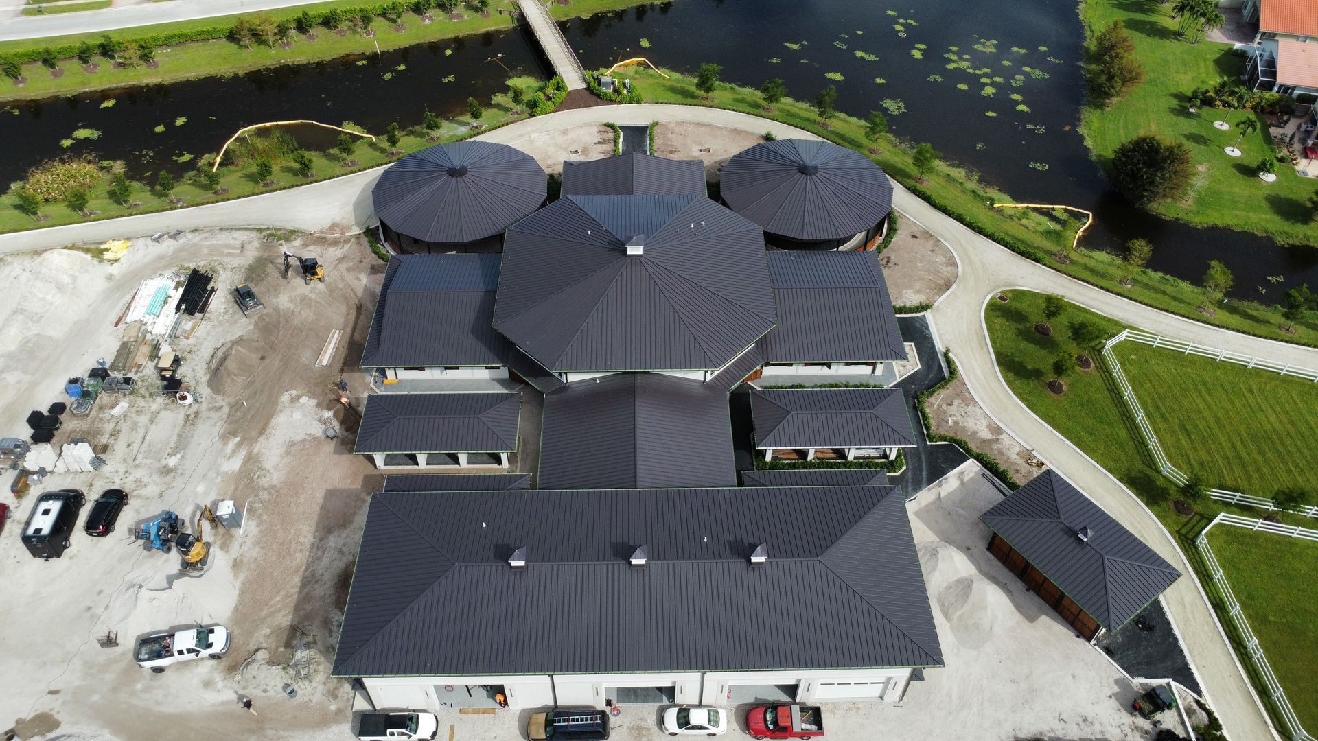 Aerial view of a large dark-roofed building beside a pond and landscaped paths
