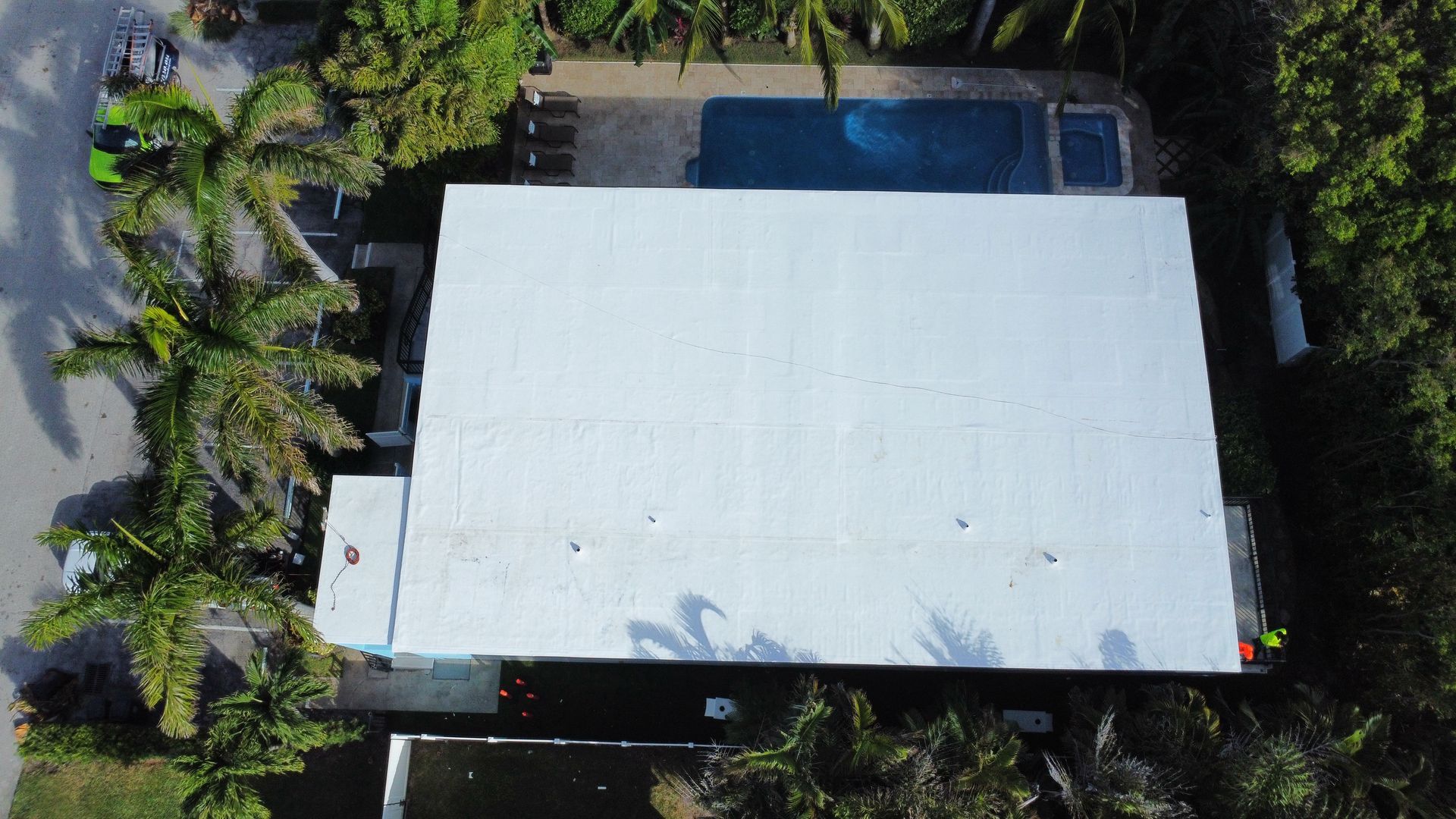 Aerial view of a white-roofed house surrounded by trees, with a blue pool at the top