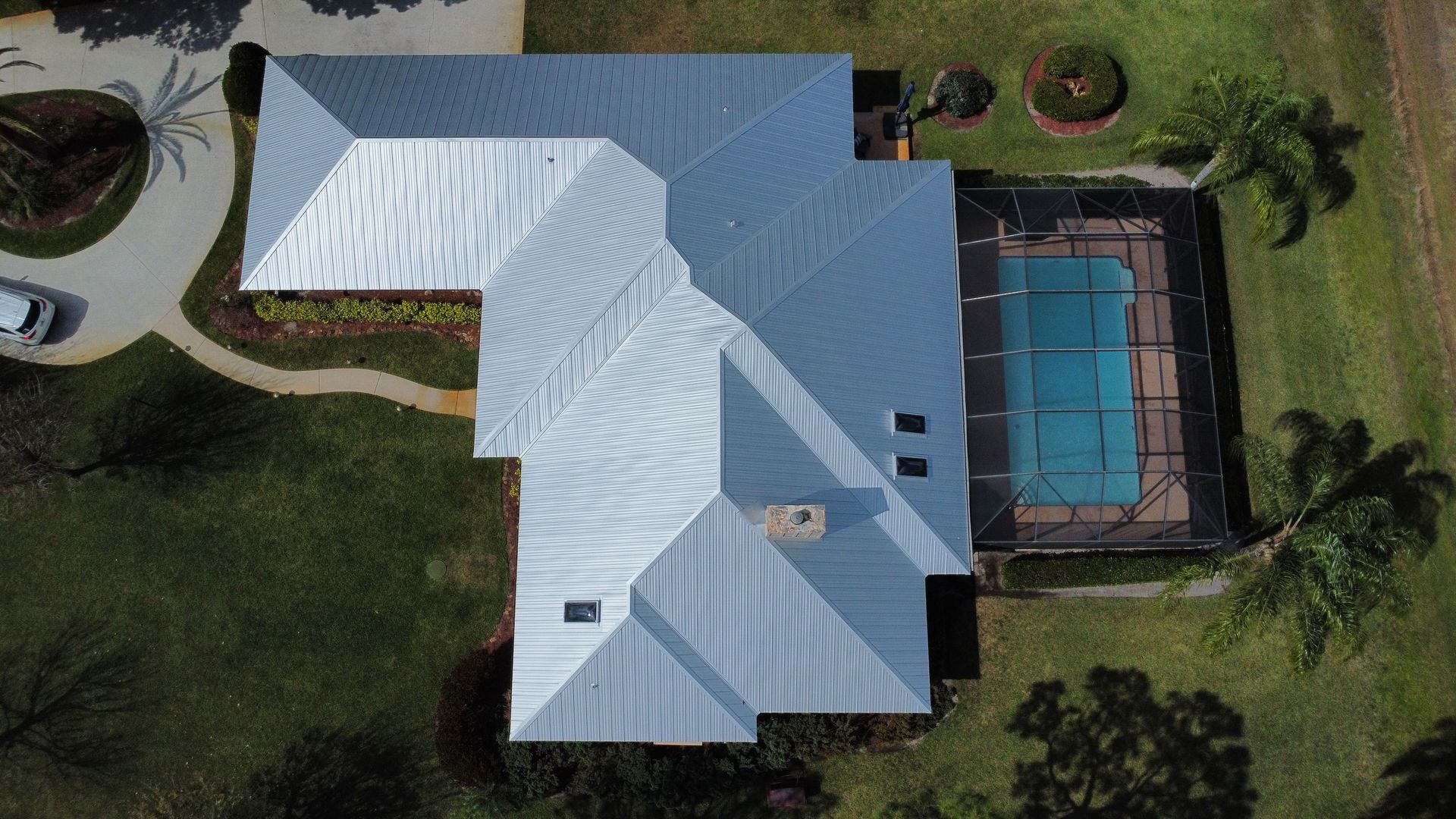 Aerial view of a white-roofed house beside a fenced blue swimming pool and green lawn.