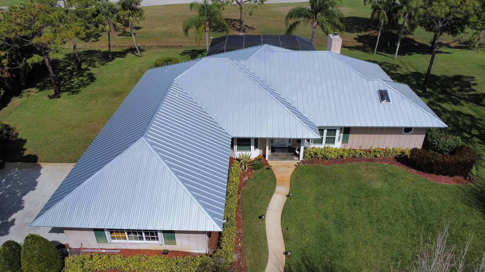 Aerial view of a house with a gray metal roof, surrounded by green lawn and a curved walkway.