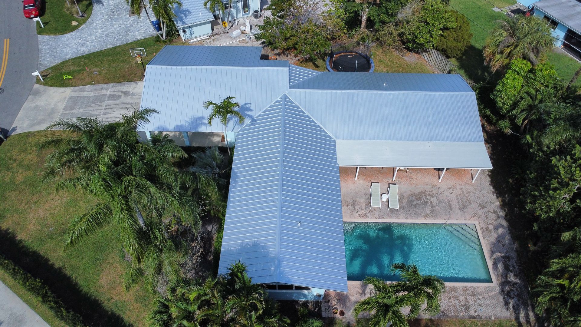 Aerial view of a house with a light blue roof, driveway, and backyard swimming pool.