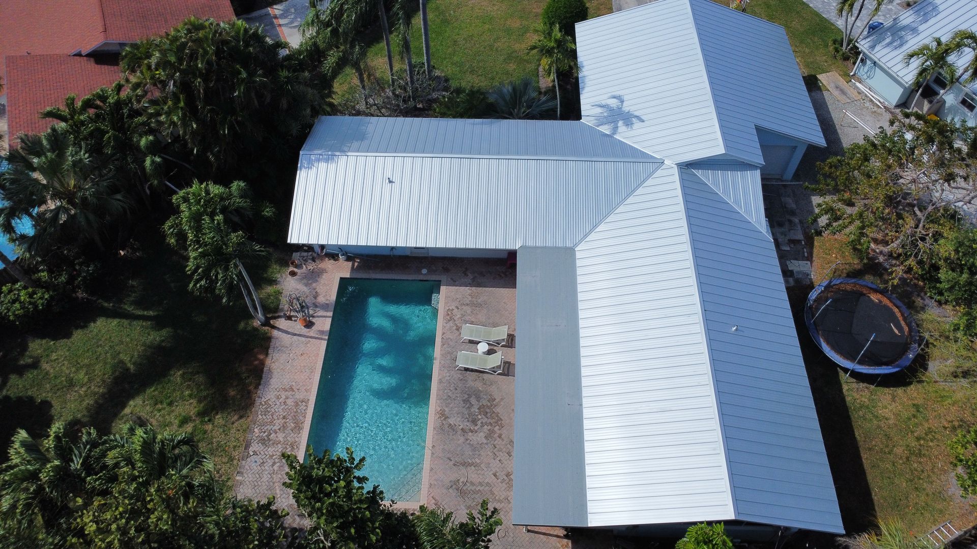 Aerial view of a house with a white roof and a backyard swimming pool.
