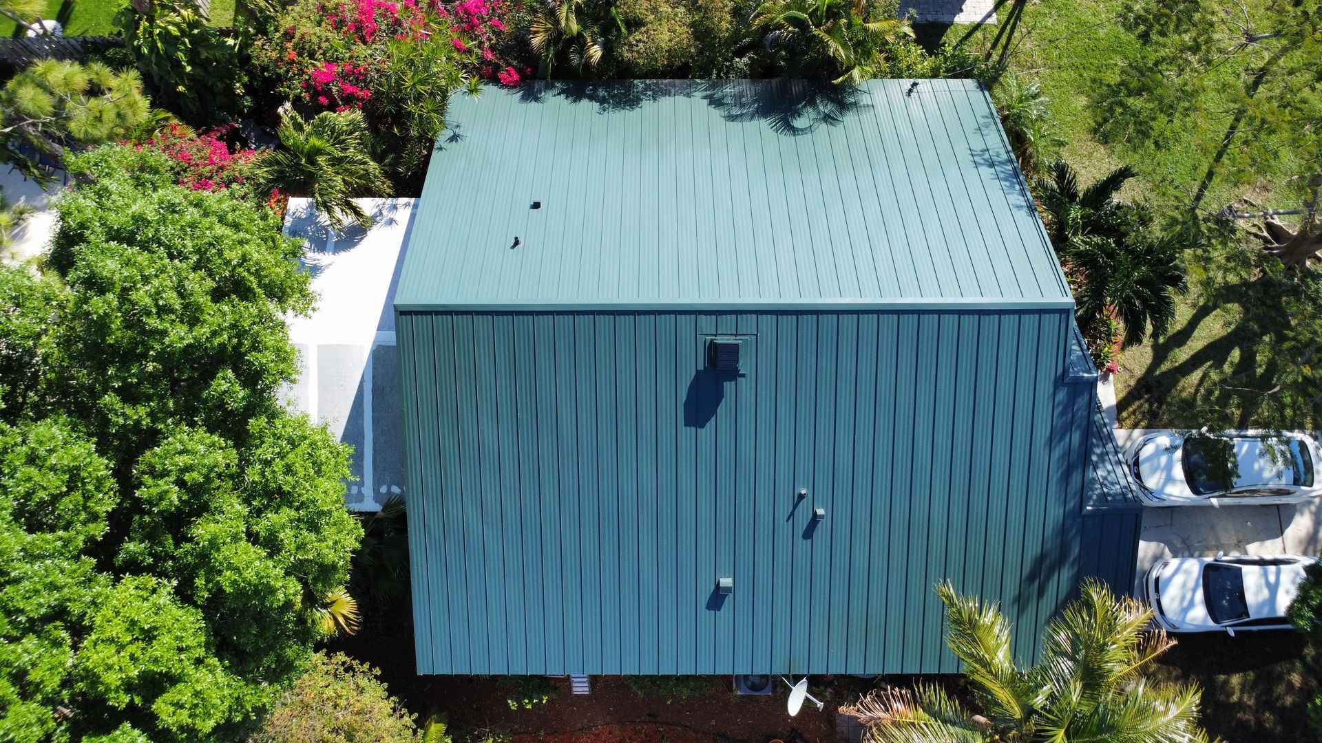Aerial view of a house with a green metal roof surrounded by trees and a driveway.