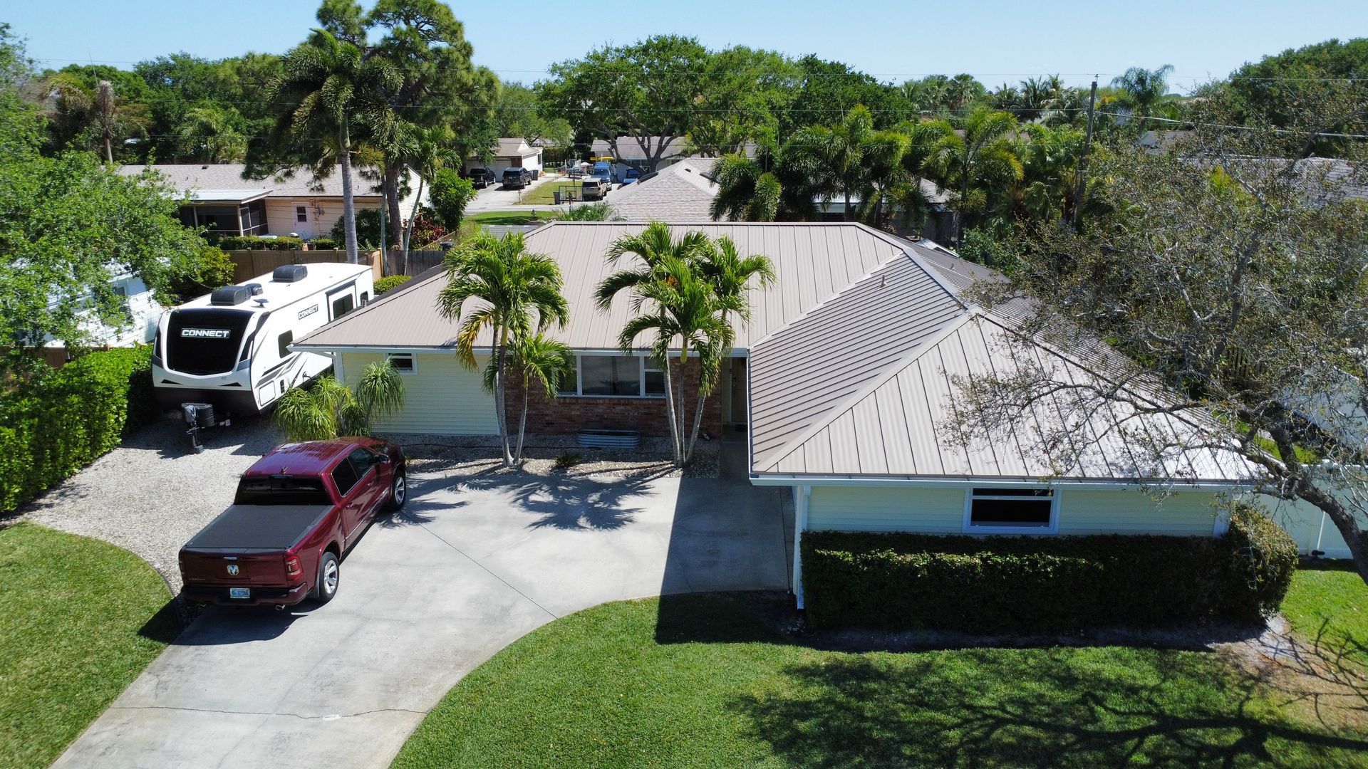 Aerial view of a suburban house with a driveway, red truck, white RV, and palm trees in the yard.