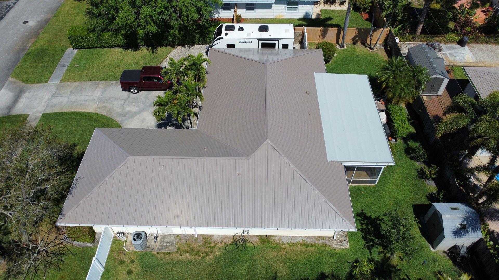 Aerial view of a house with a gray roof, driveway, trees, and a parked vehicle in the yard
