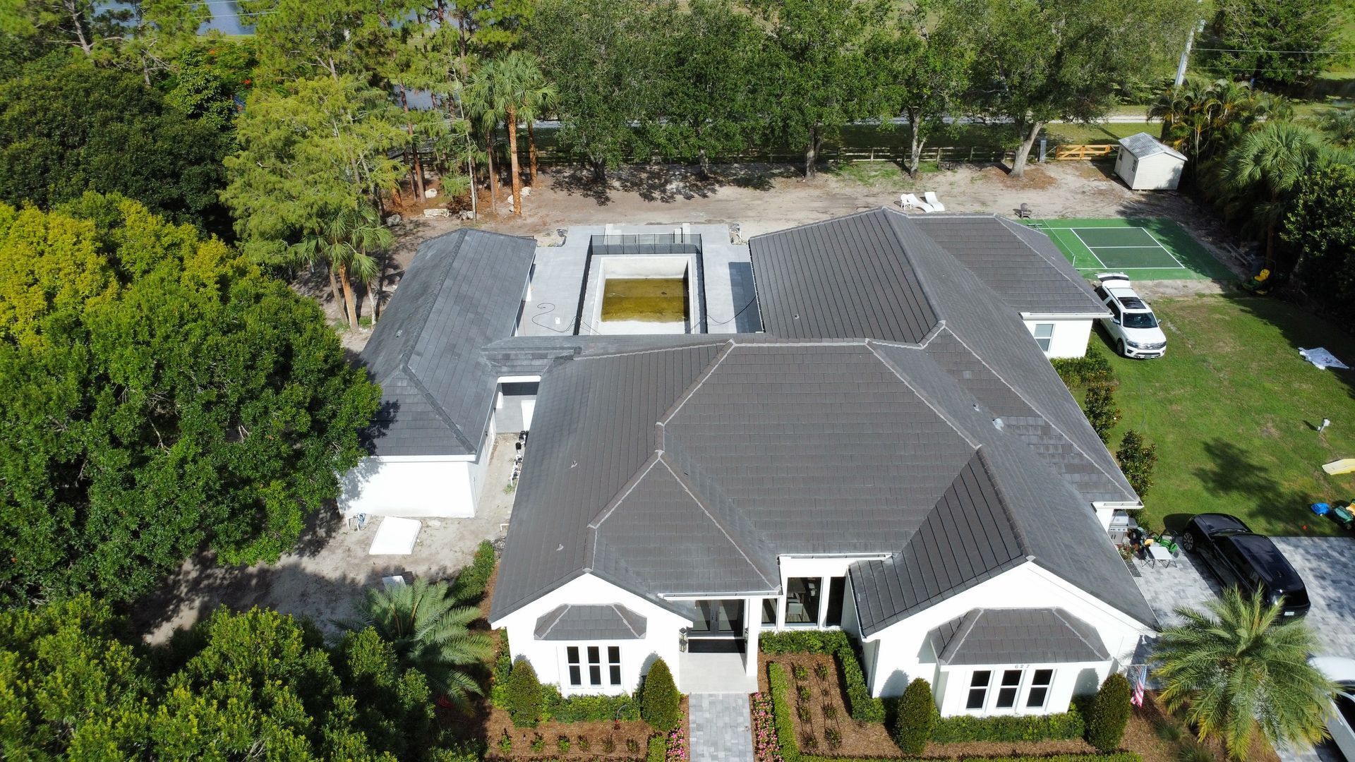 Aerial view of a large white house with a gray roof, surrounded by trees and a yard.
