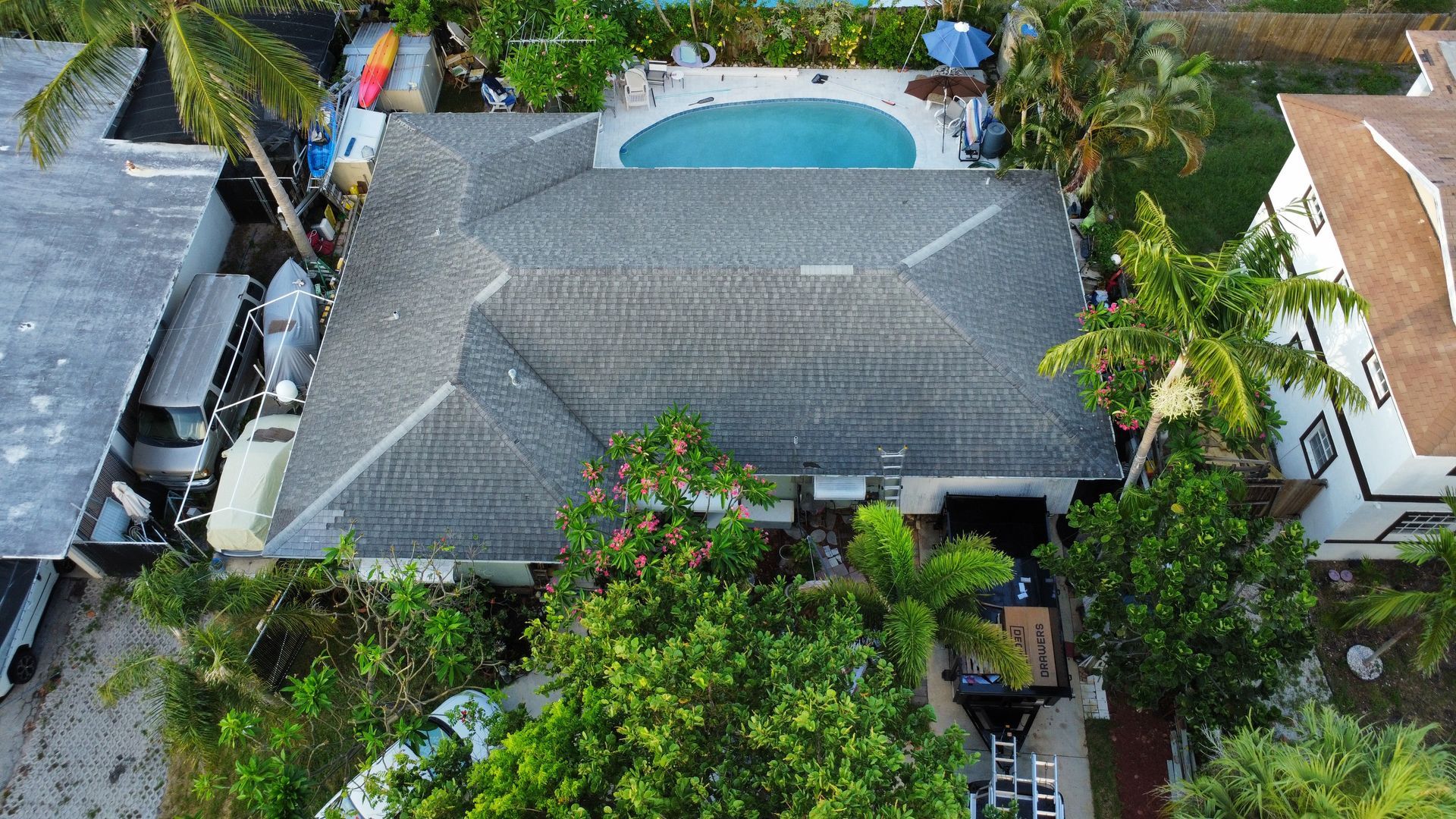 Aerial view of a house with a gray roof, surrounded by lush trees and a backyard pool.