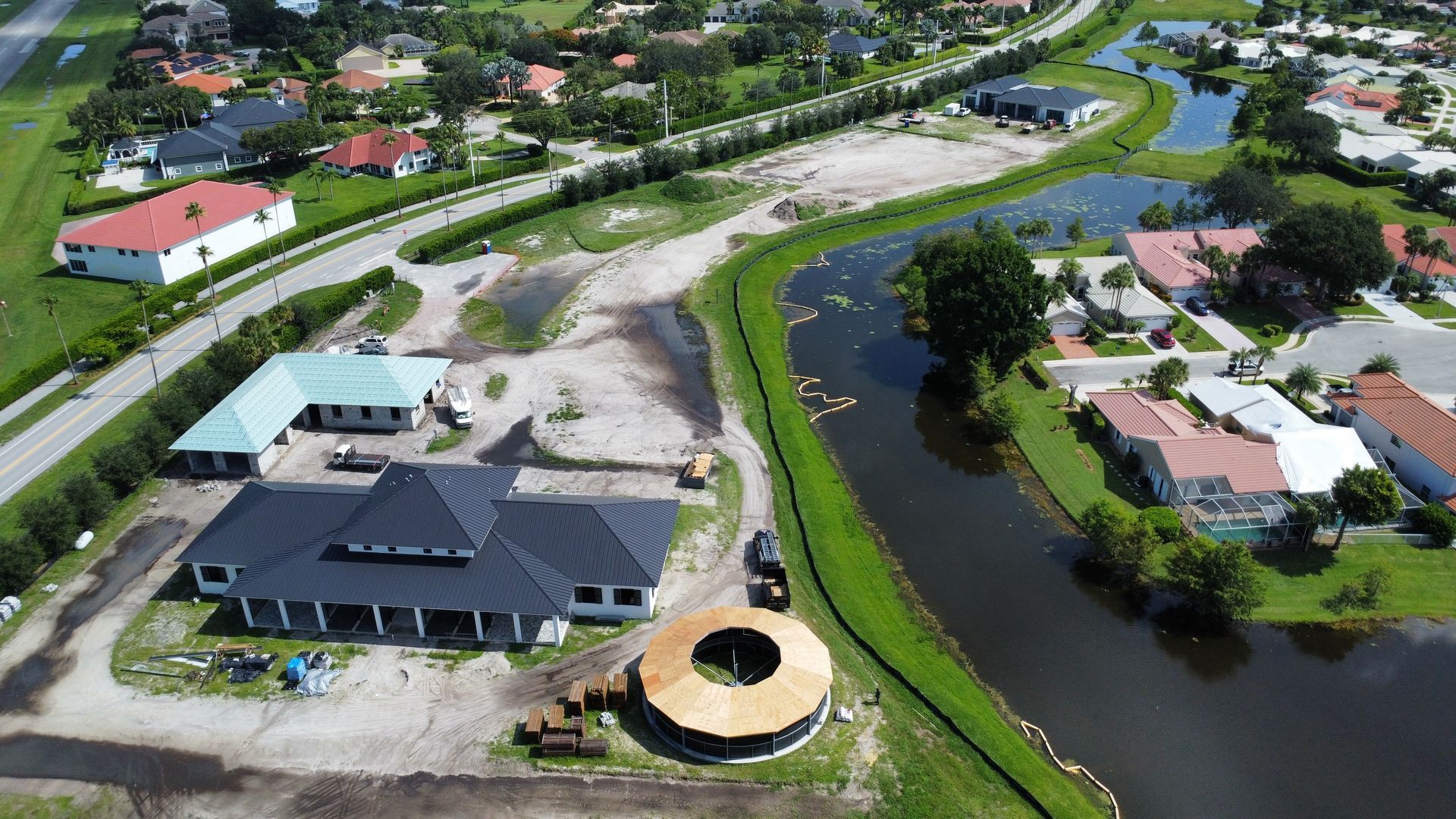 Aerial view of a neighborhood with houses, winding canal, roads, and a building under construction.