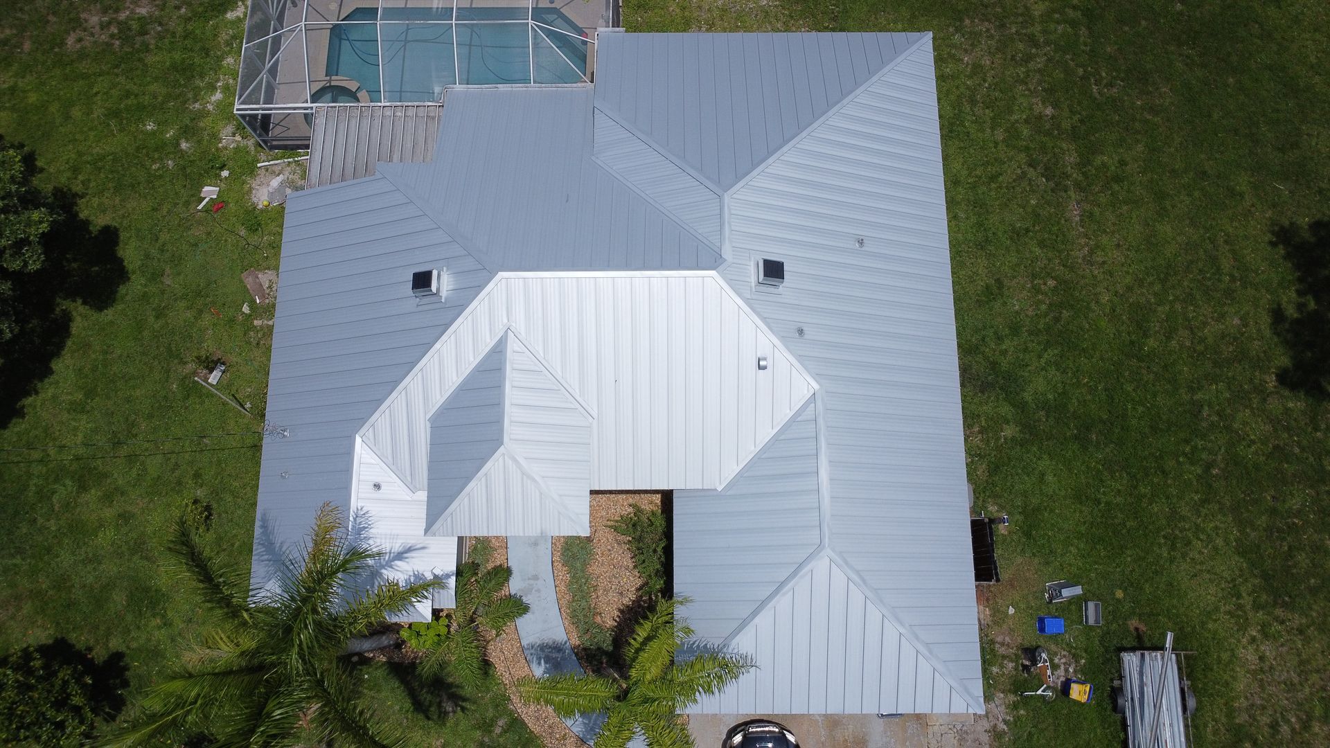 Aerial view of a house with a light gray roof and small backyard, surrounded by trees and grass.