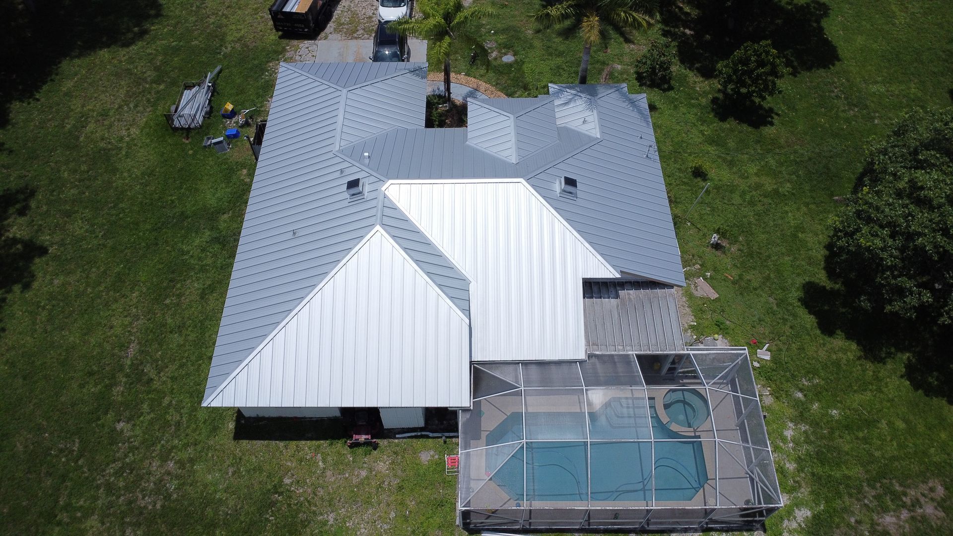 Aerial view of a house with a white roof and a screened-in backyard pool.