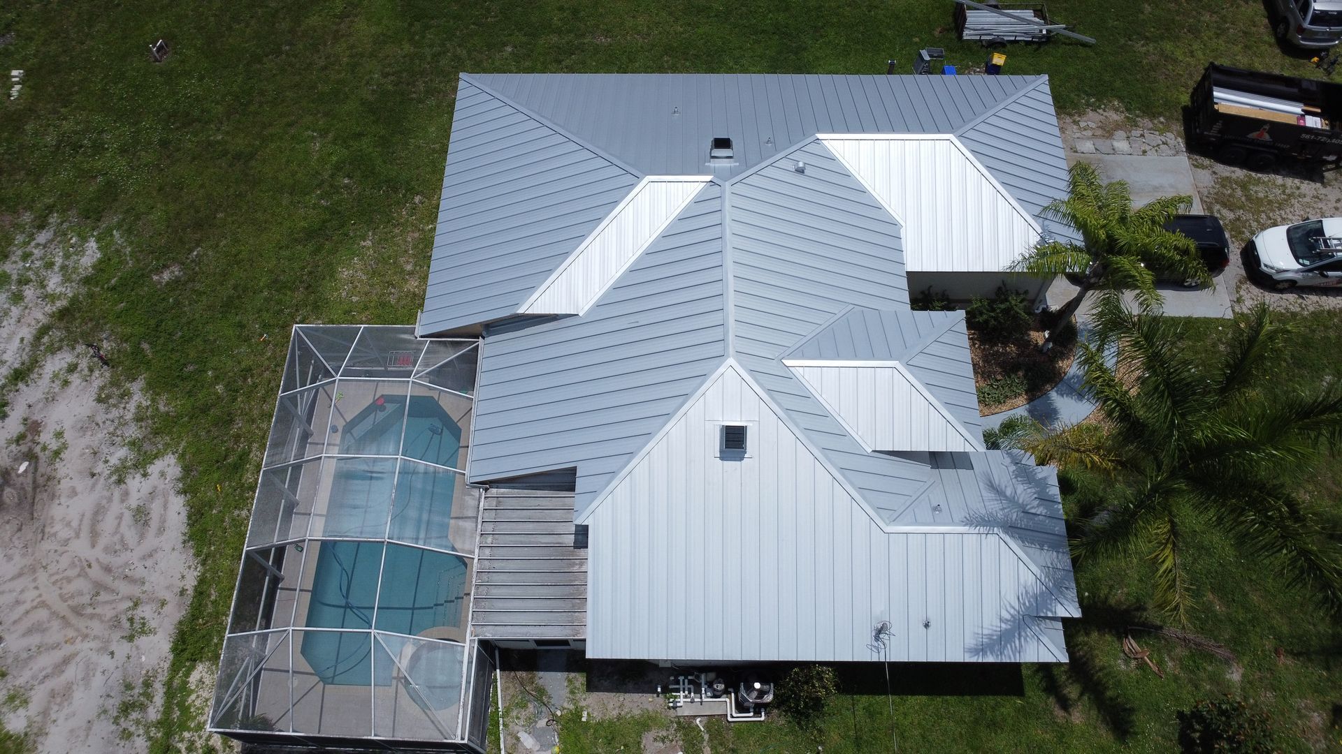 Aerial view of a house with a gray metal roof and screened pool enclosure in a grassy yard.