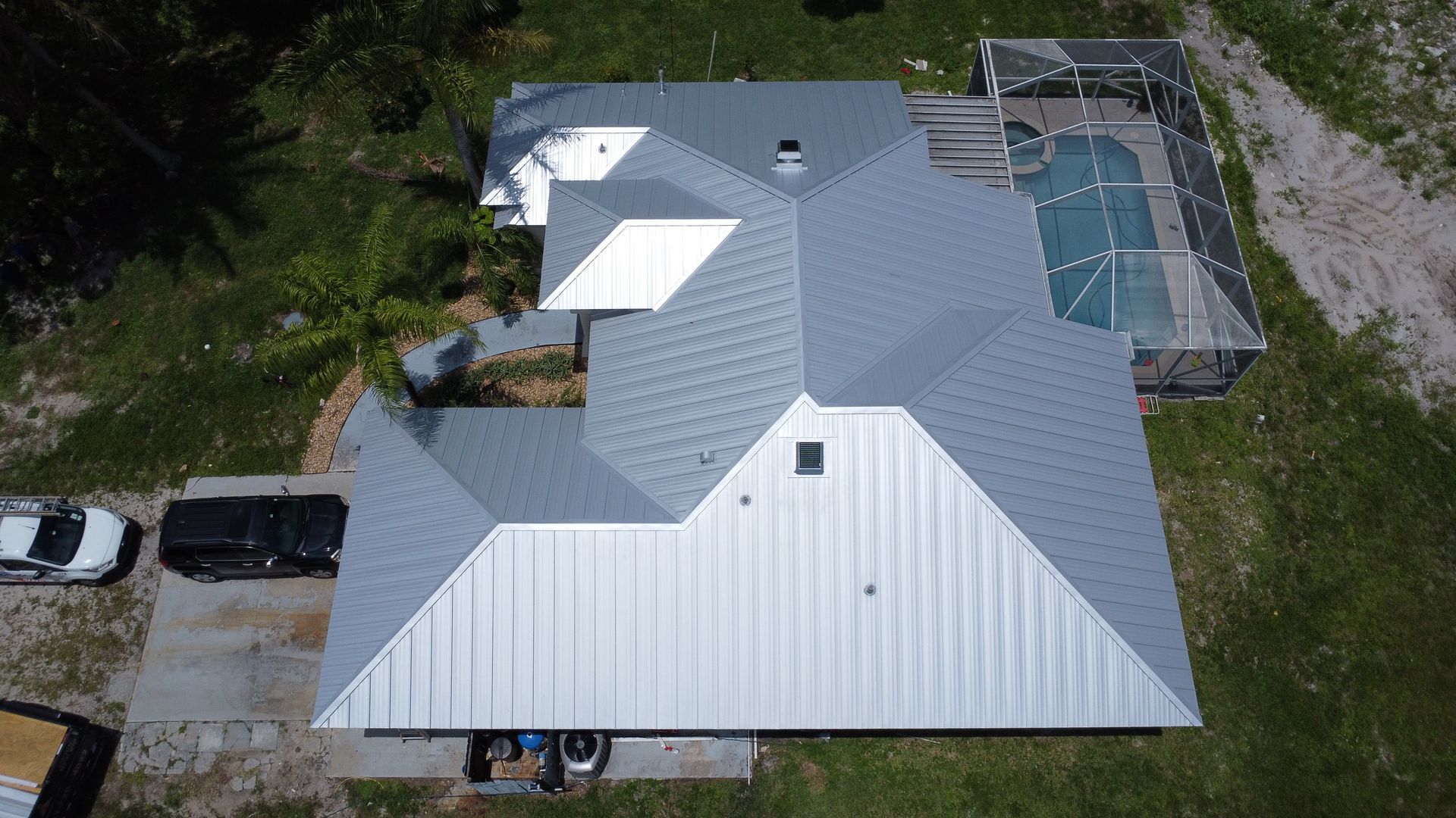 Aerial view of a house with a light gray metal roof and backyard pool surrounded by trees