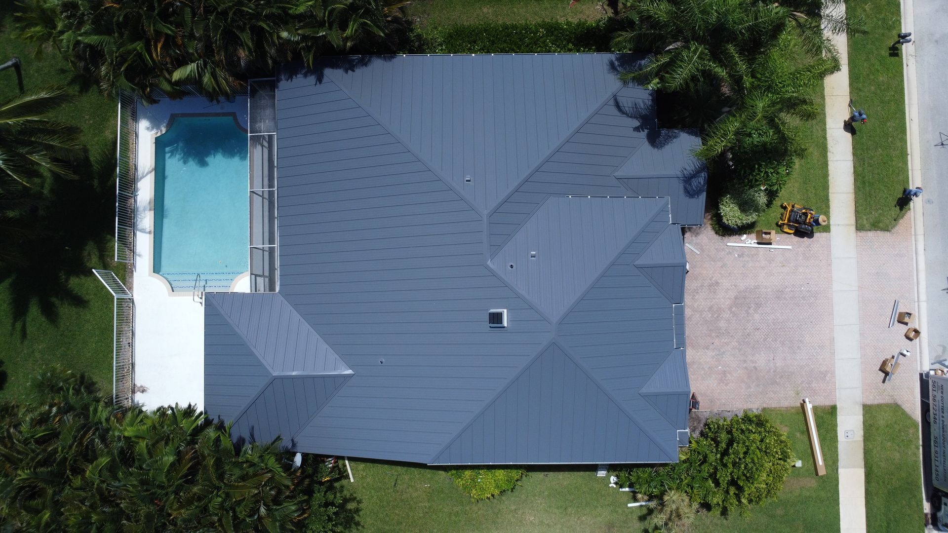 Aerial view of a house with a gray roof, pool on the left, and driveway on the right.