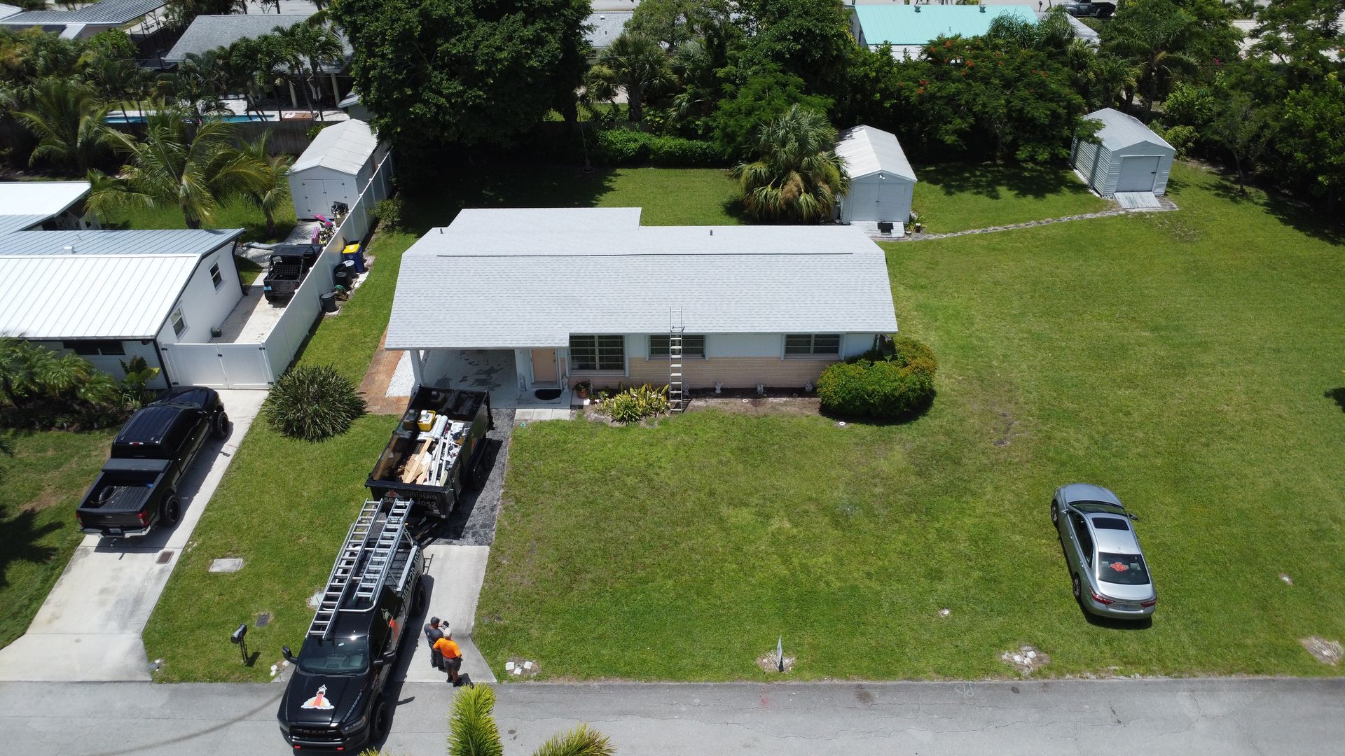 Aerial view of a single-story house with a large green lawn and several parked vehicles nearby.