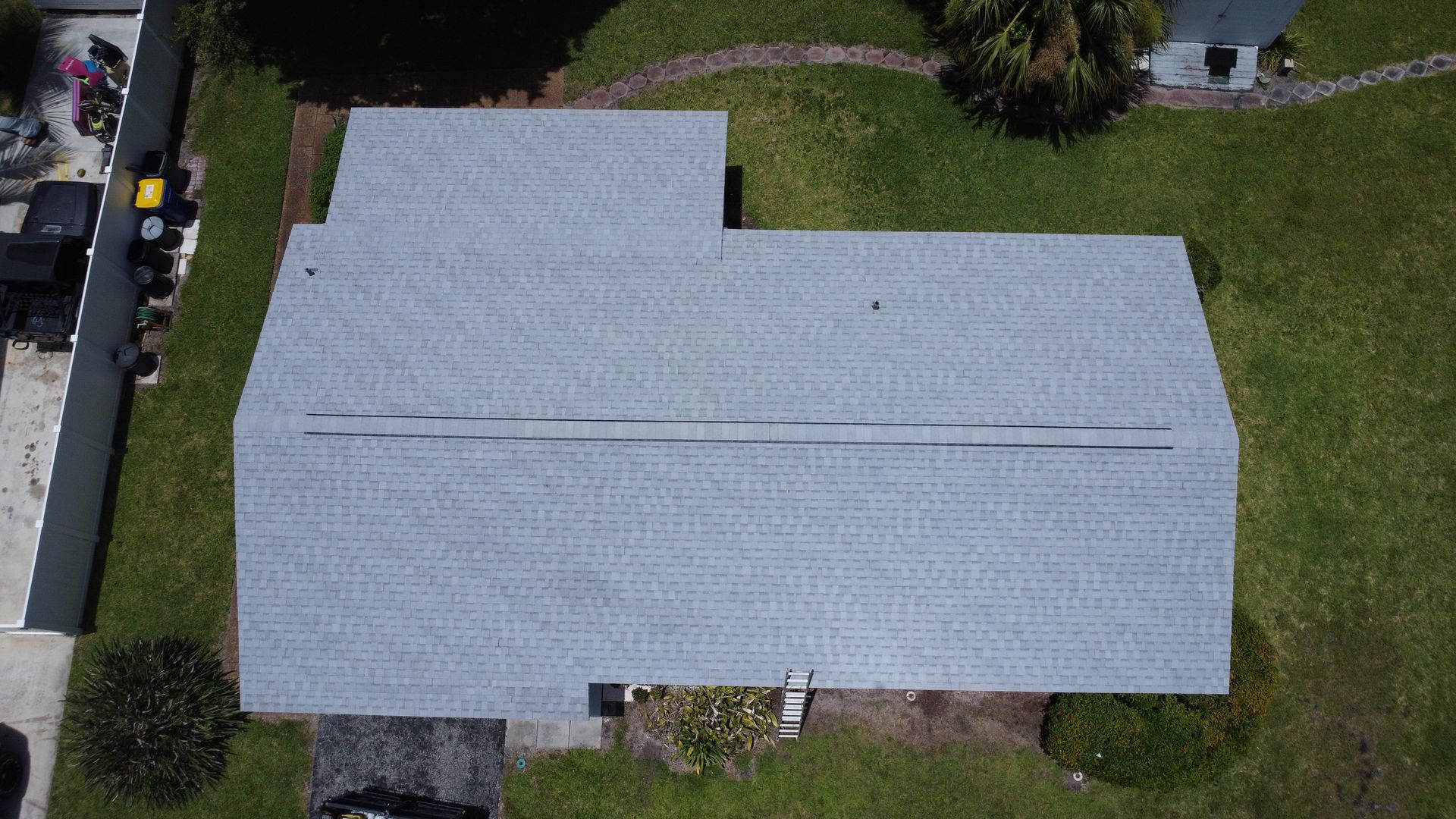 Aerial view of a gray-roofed house with a grassy yard and driveway.