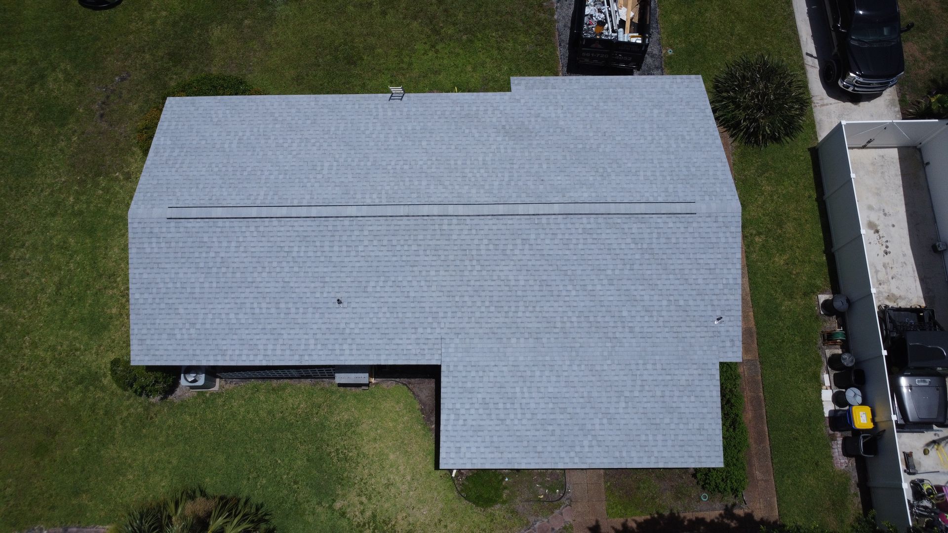Aerial view of a gray-roofed house with a front lawn and a driveway with parked vehicles.