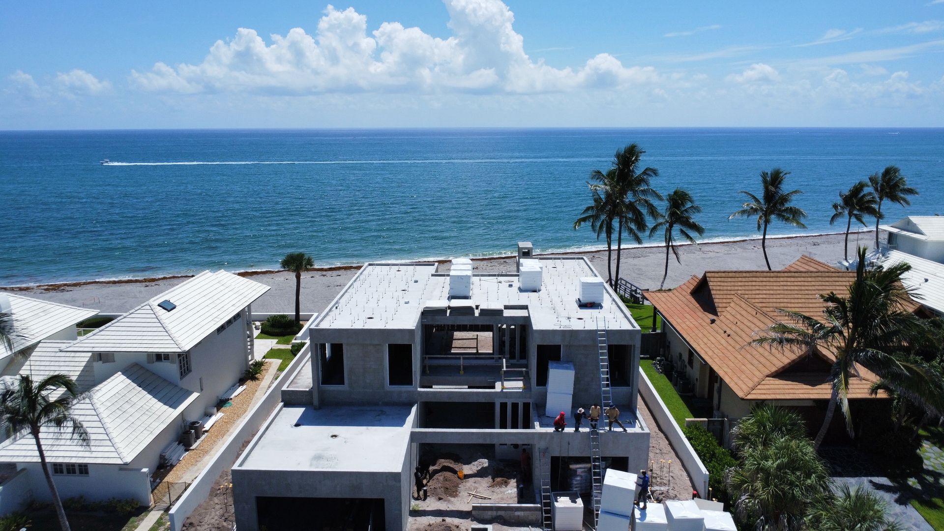 Coastal view of modern beachfront homes, palm trees, and the blue ocean under a bright sky