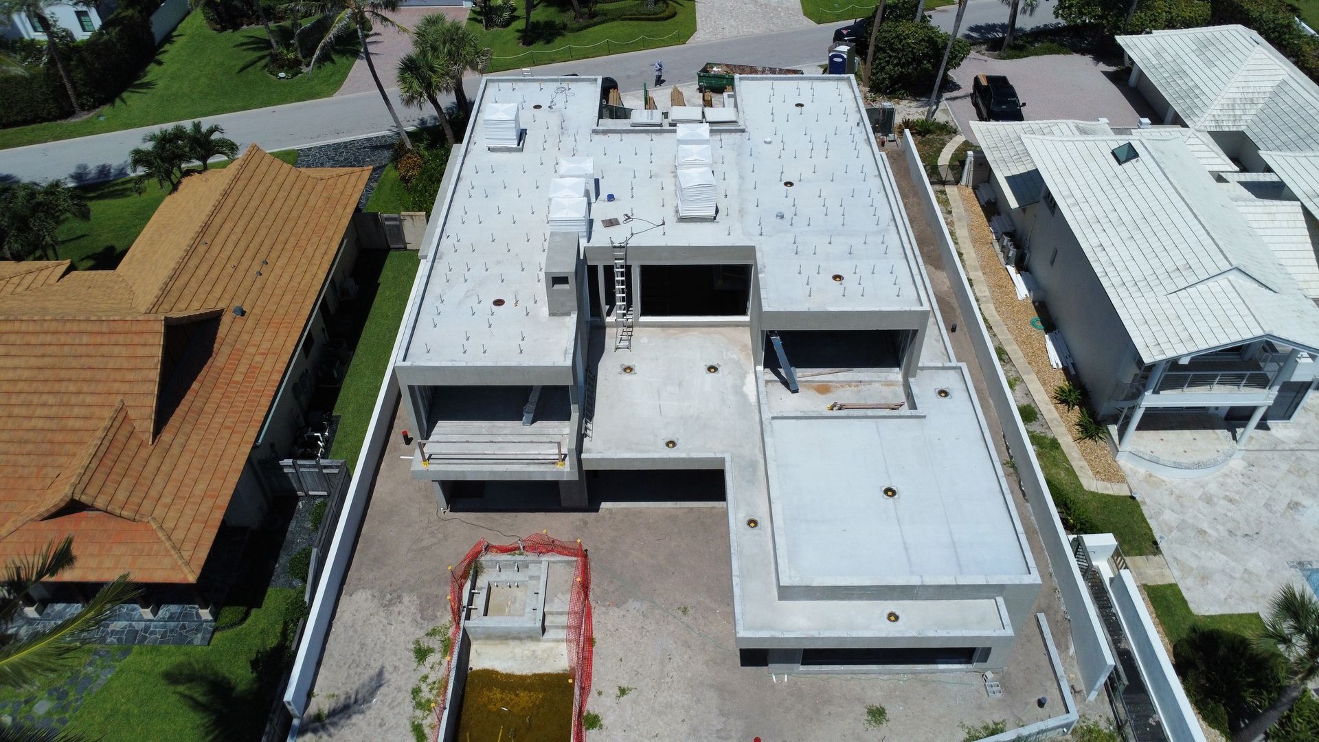 Aerial view of a modern white-roofed house with a driveway and neighboring homes.