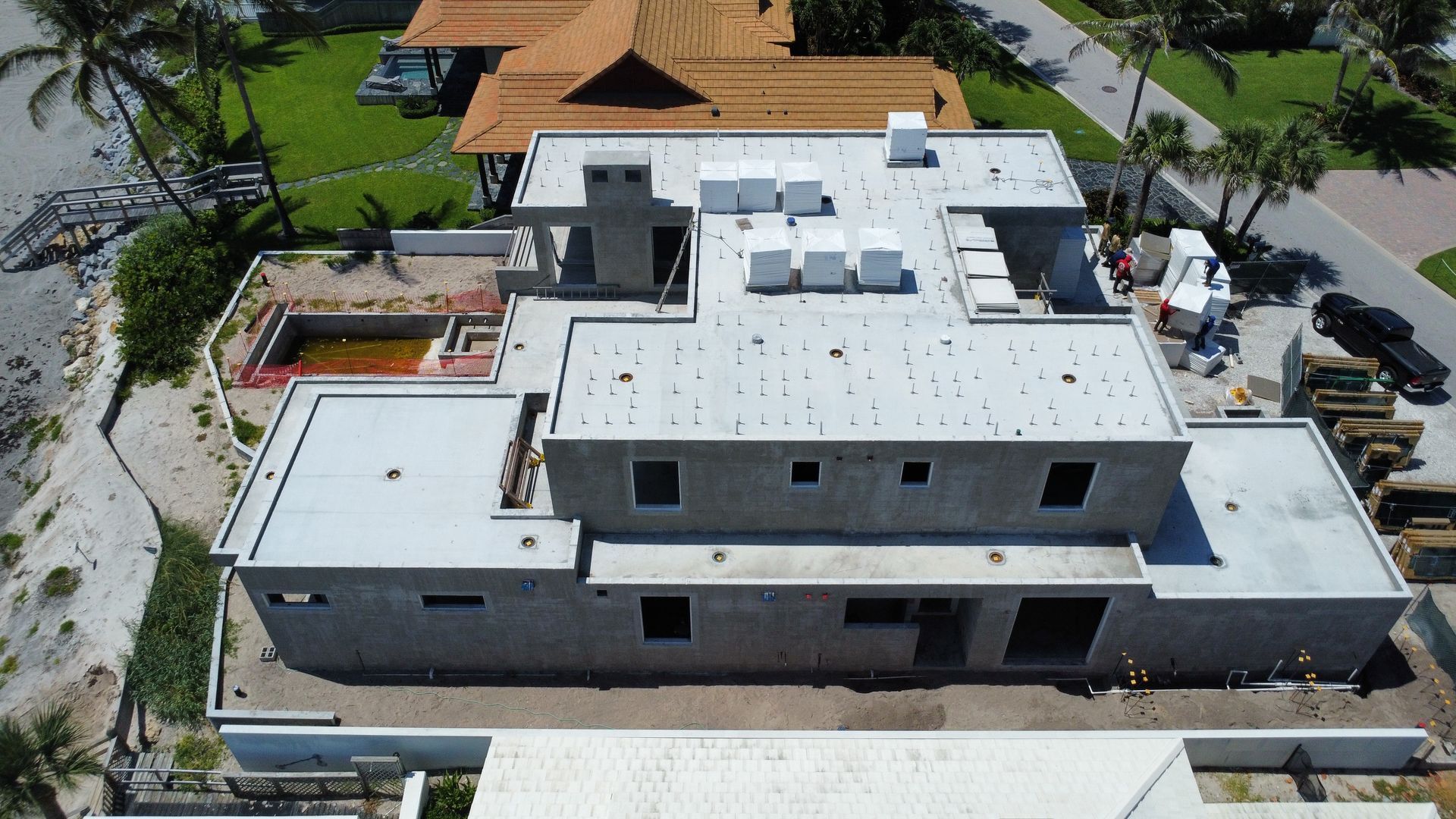 Aerial view of a large white modern house under construction beside neighboring homes and a street