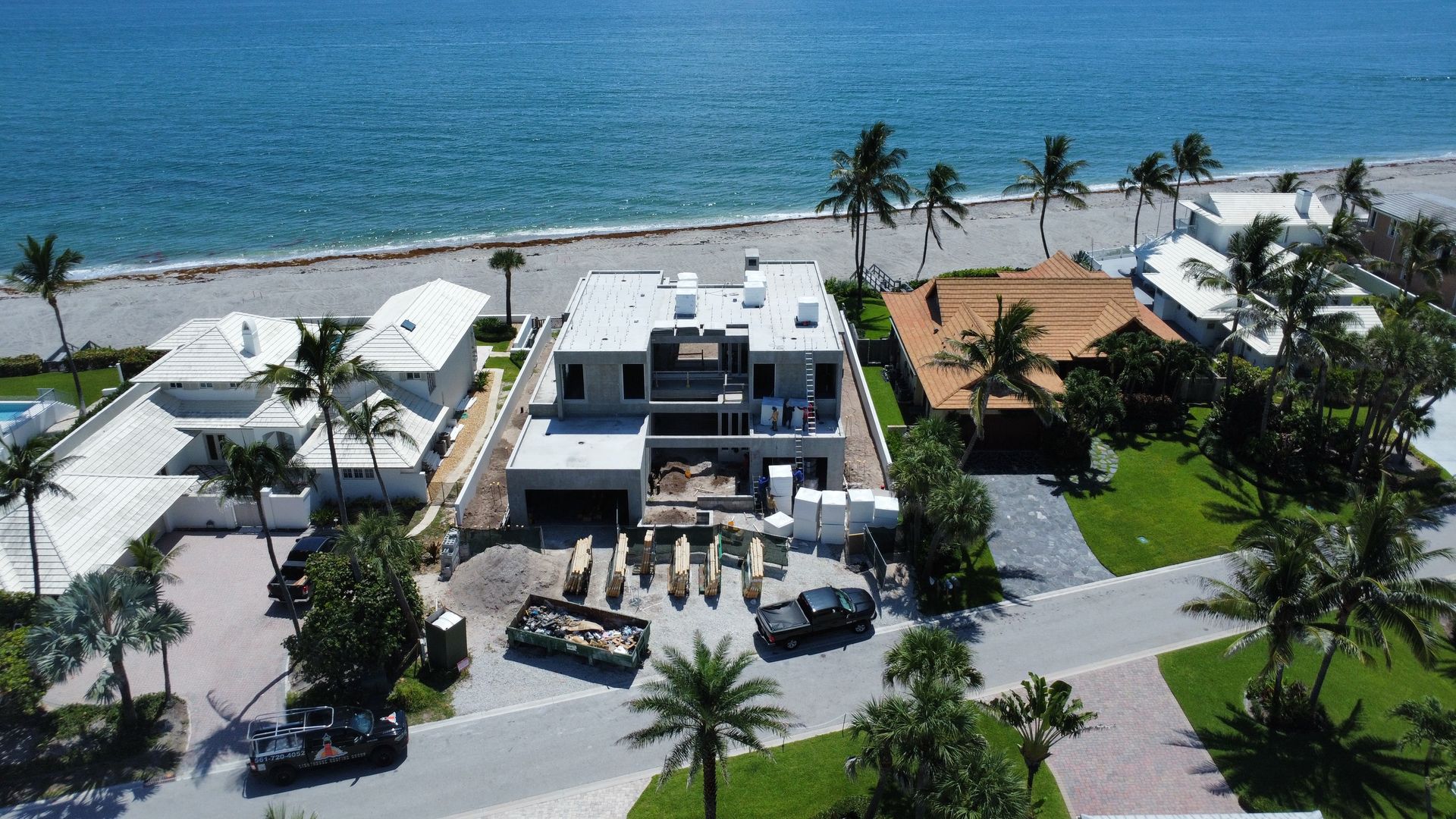Aerial view of a modern beachfront house with palm trees and ocean behind it.
