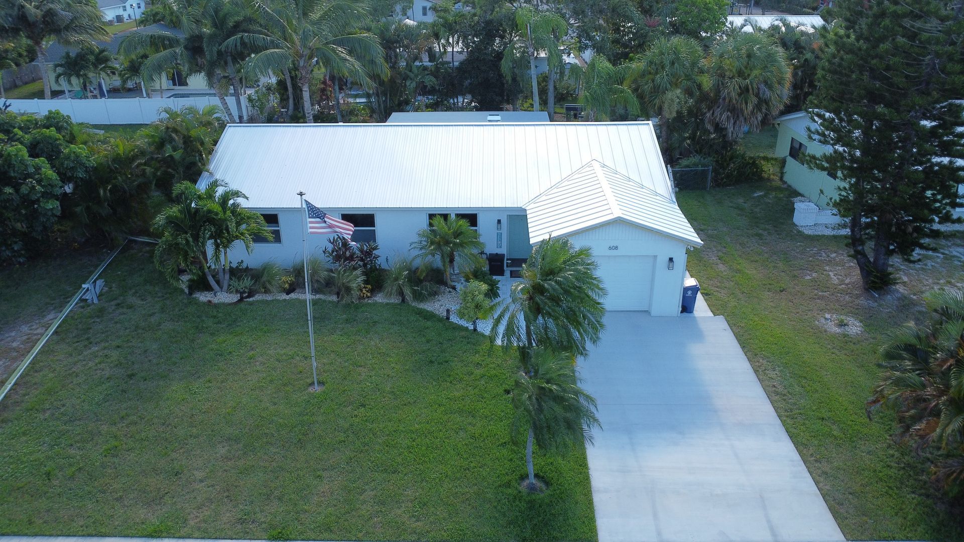 Aerial view of a white house with a driveway, surrounded by trees and a grassy yard.