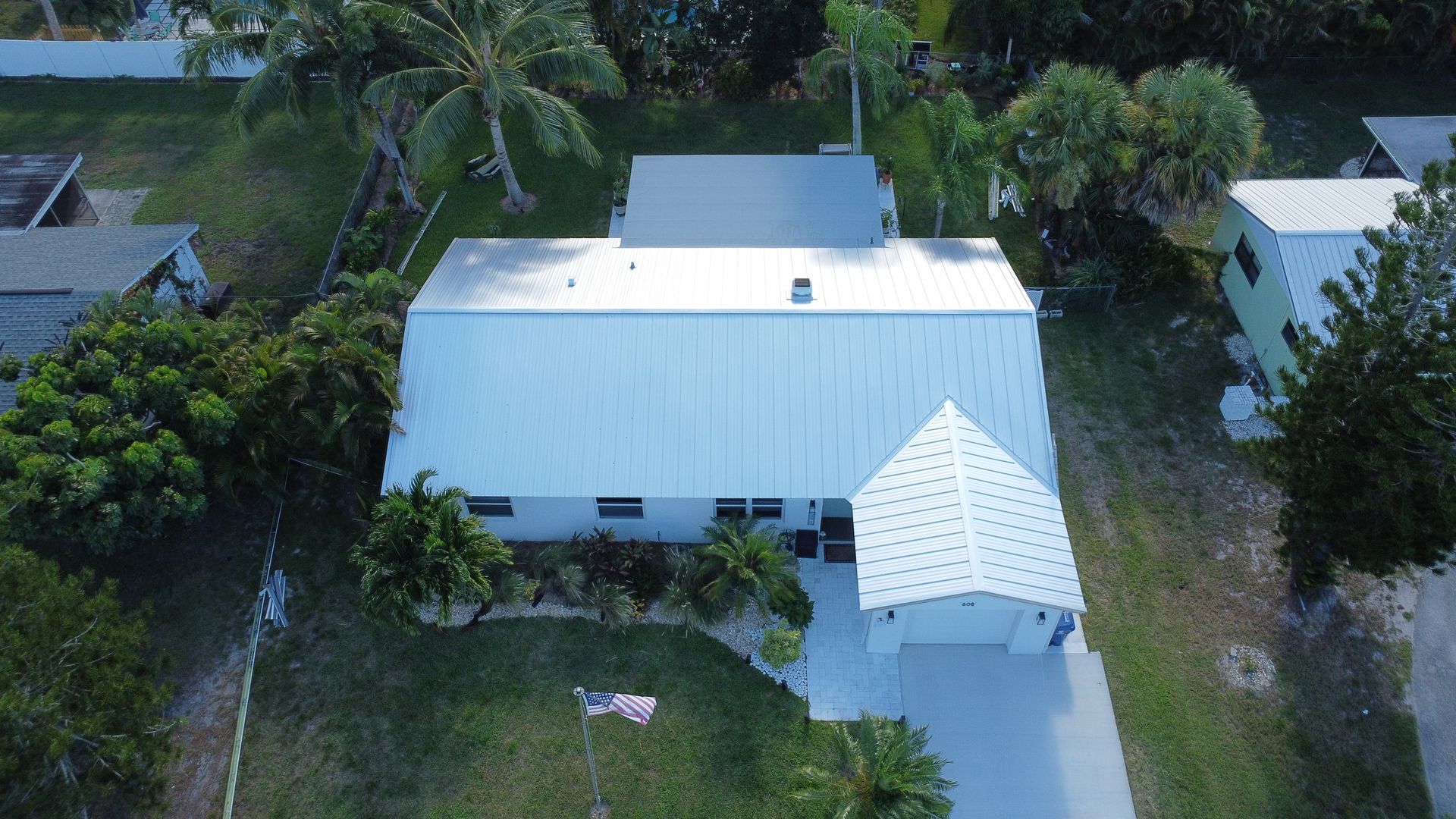 Aerial view of a white house with a driveway, surrounded by trees and greenery.