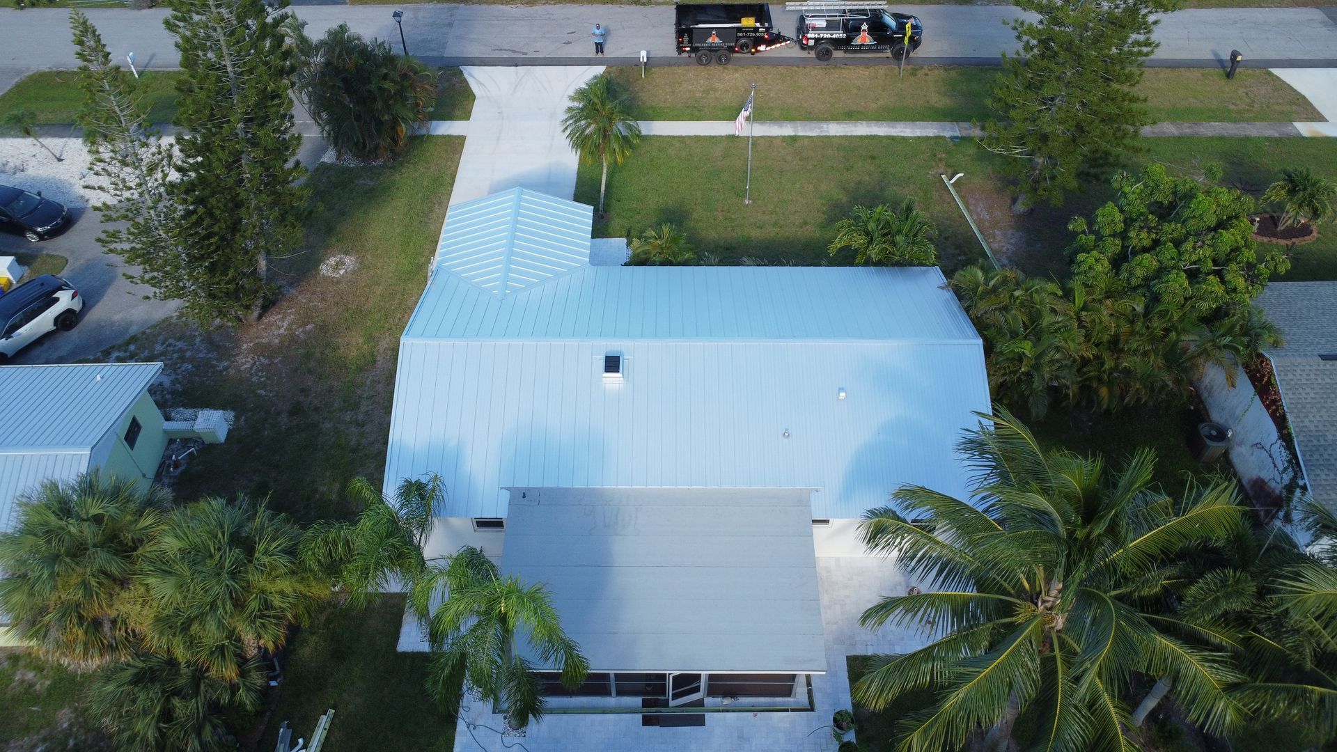 Aerial view of a white-roofed house with a long driveway and surrounding trees.