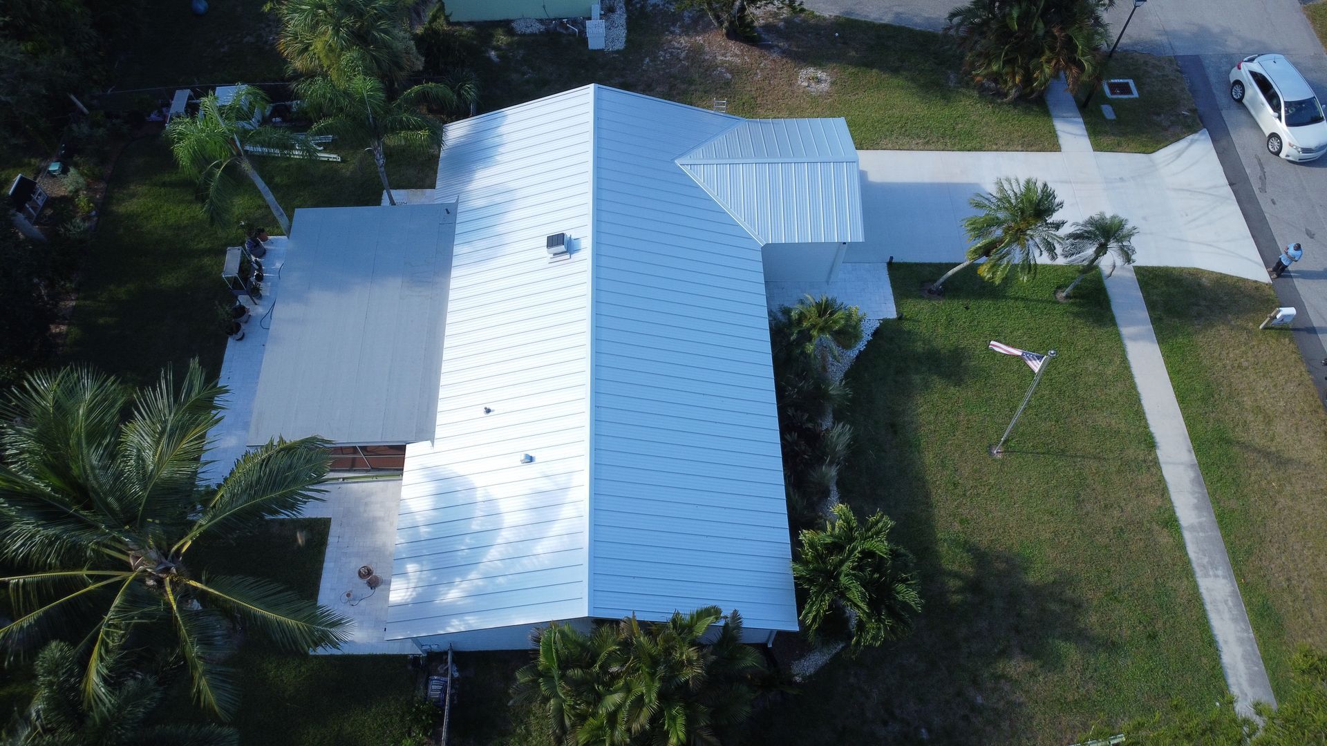 Aerial view of a white-roofed house with palm trees, driveway, and green lawn.