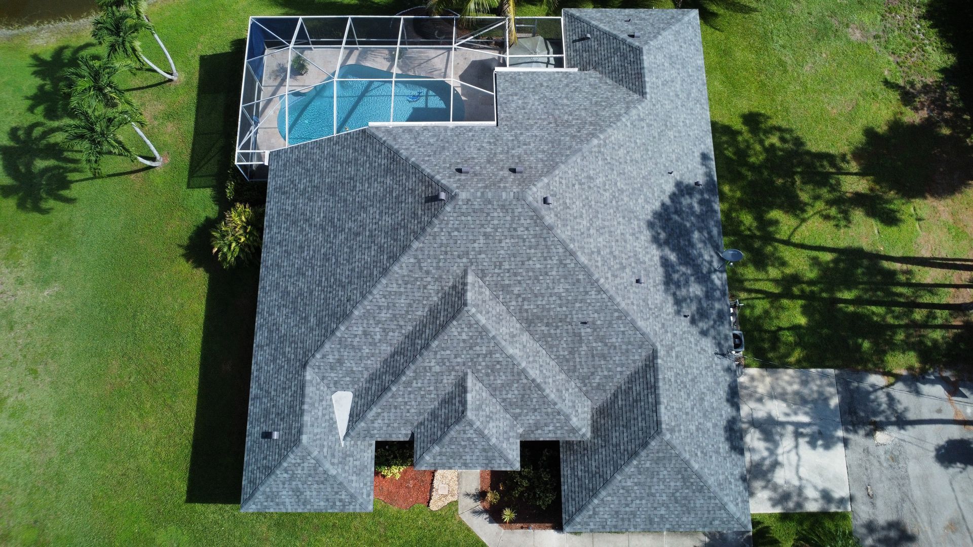 Aerial view of a gray-roofed house with a backyard pool and green lawn.