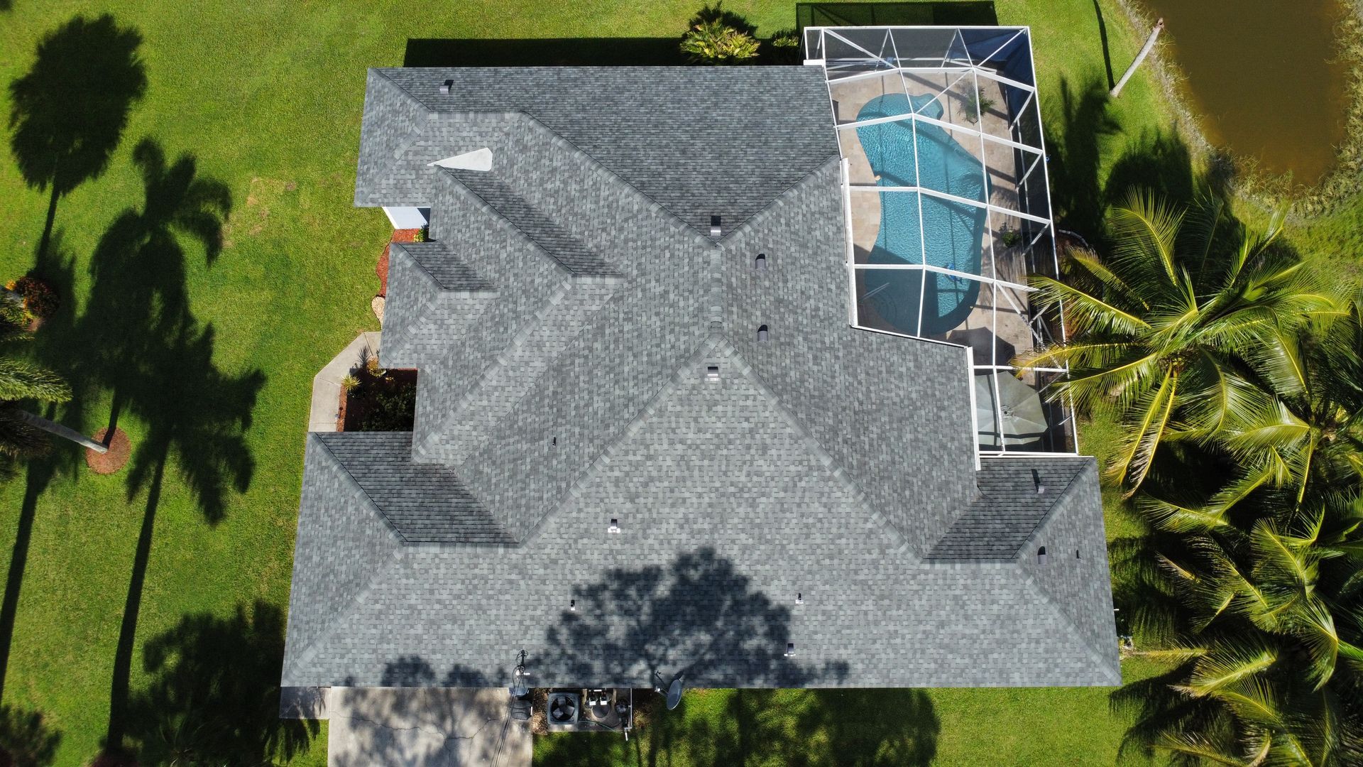 Aerial view of a gray-roofed house with a screened swimming pool and surrounding green lawn.