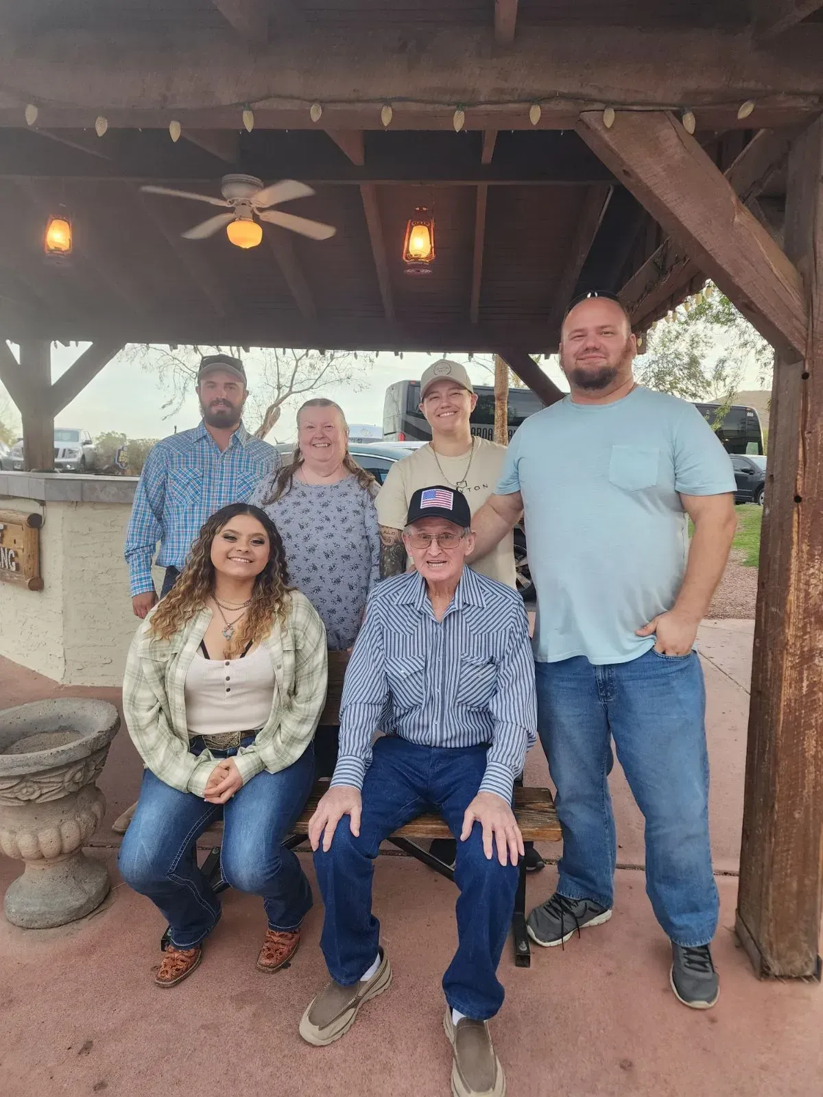 Group of six people posing under a wooden pavilion, with string lights and rustic decor.