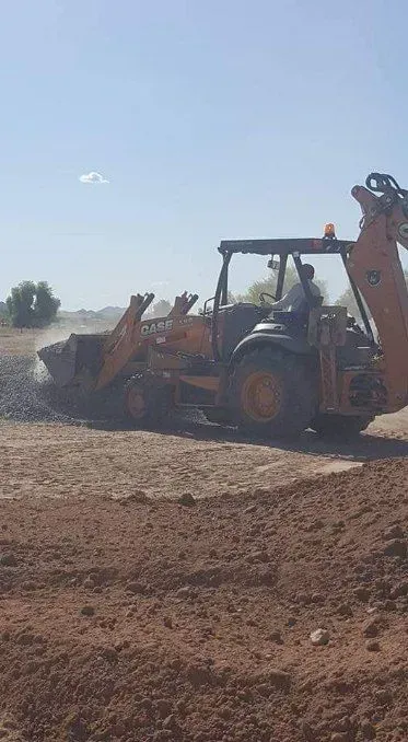 Orange backhoe loader working on a dirt road under a clear sky
