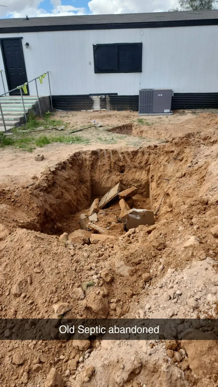 Large dirt hole in front of a white building, with exposed debris and text reading “Old septic abandoned.”